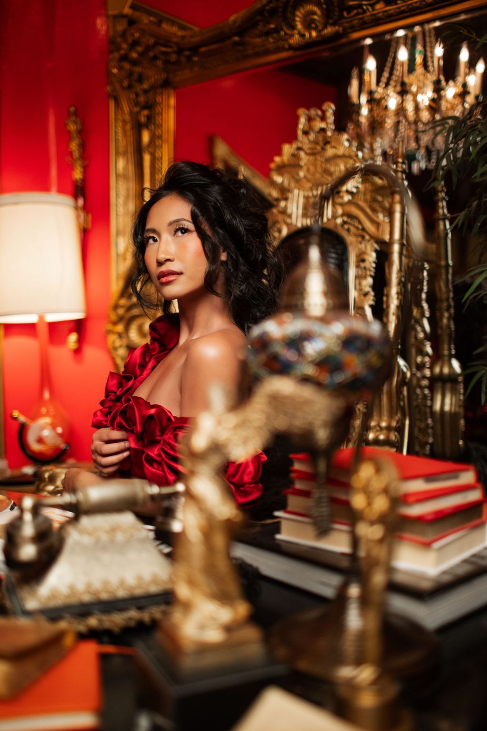Elegant portrait in opulent red room with vintage decor, gold mirrors, and dramatic lighting.