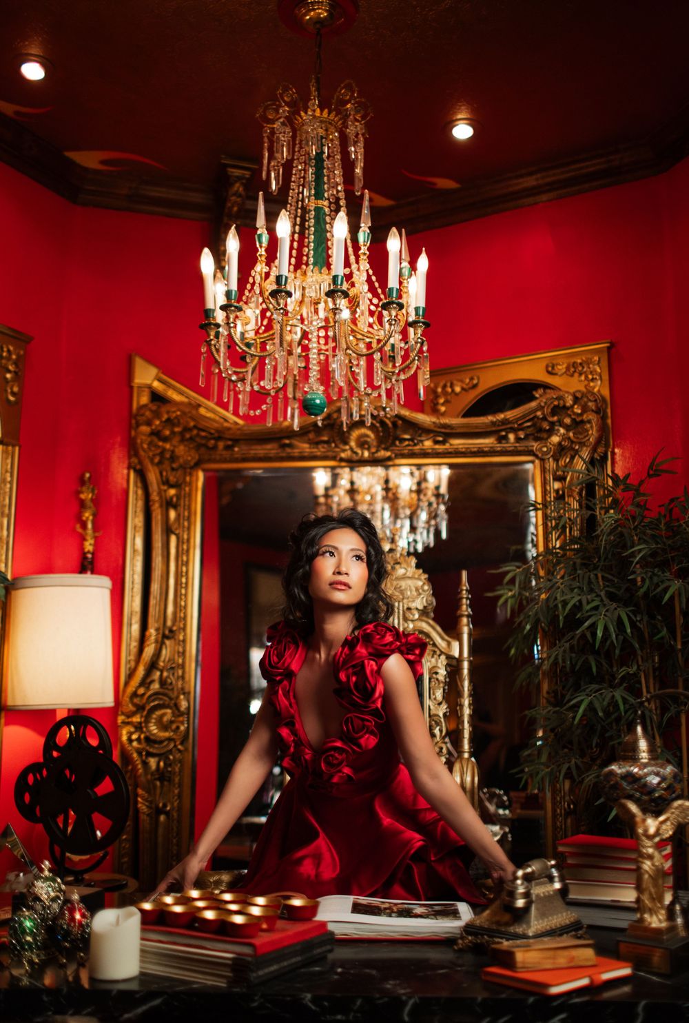 An elegant scene with an ornate chandelier, gilt mirror, and red walls featuring someone in a scarlet dress.