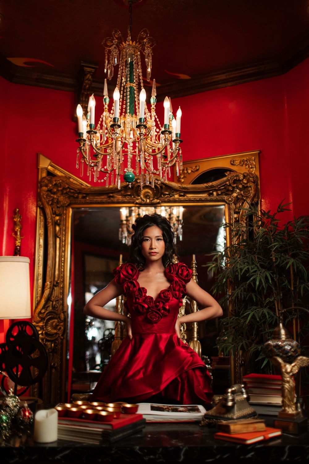 Glamorous fashion scene with ornate gold mirror, crystal chandelier and red walls in luxurious interior setting.