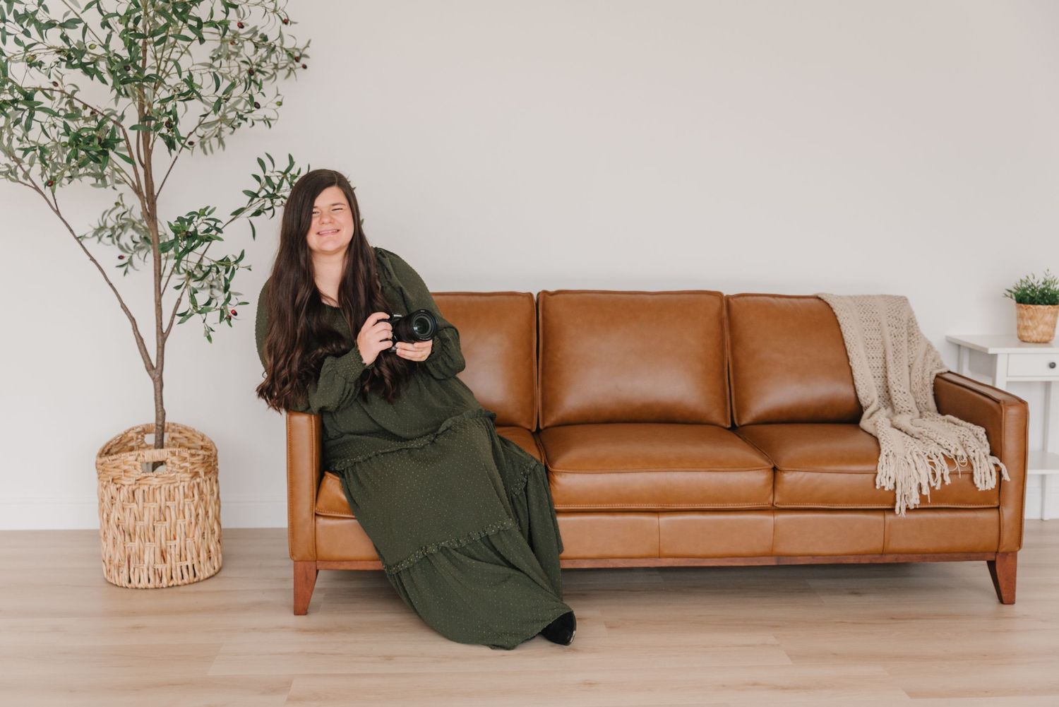 Interior scene with brown leather sofa, potted plant and figure in long green dress sitting in minimalist living room.