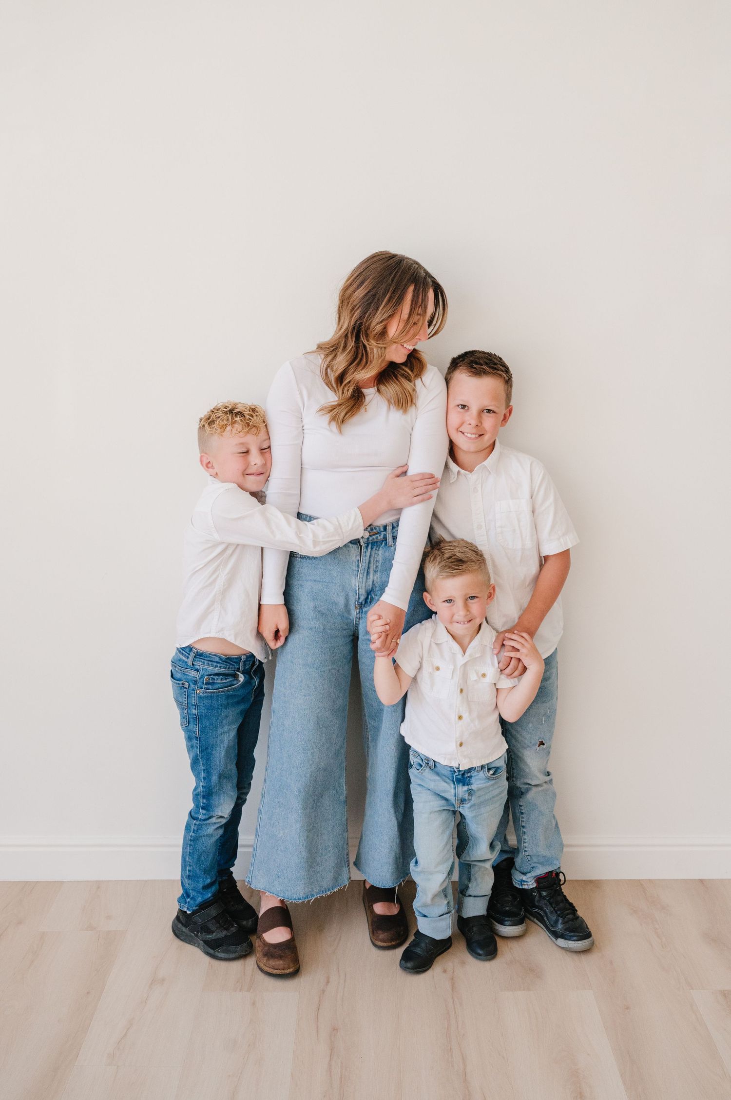 Family portrait in matching white and denim outfits standing together against neutral wall with light wood floors.