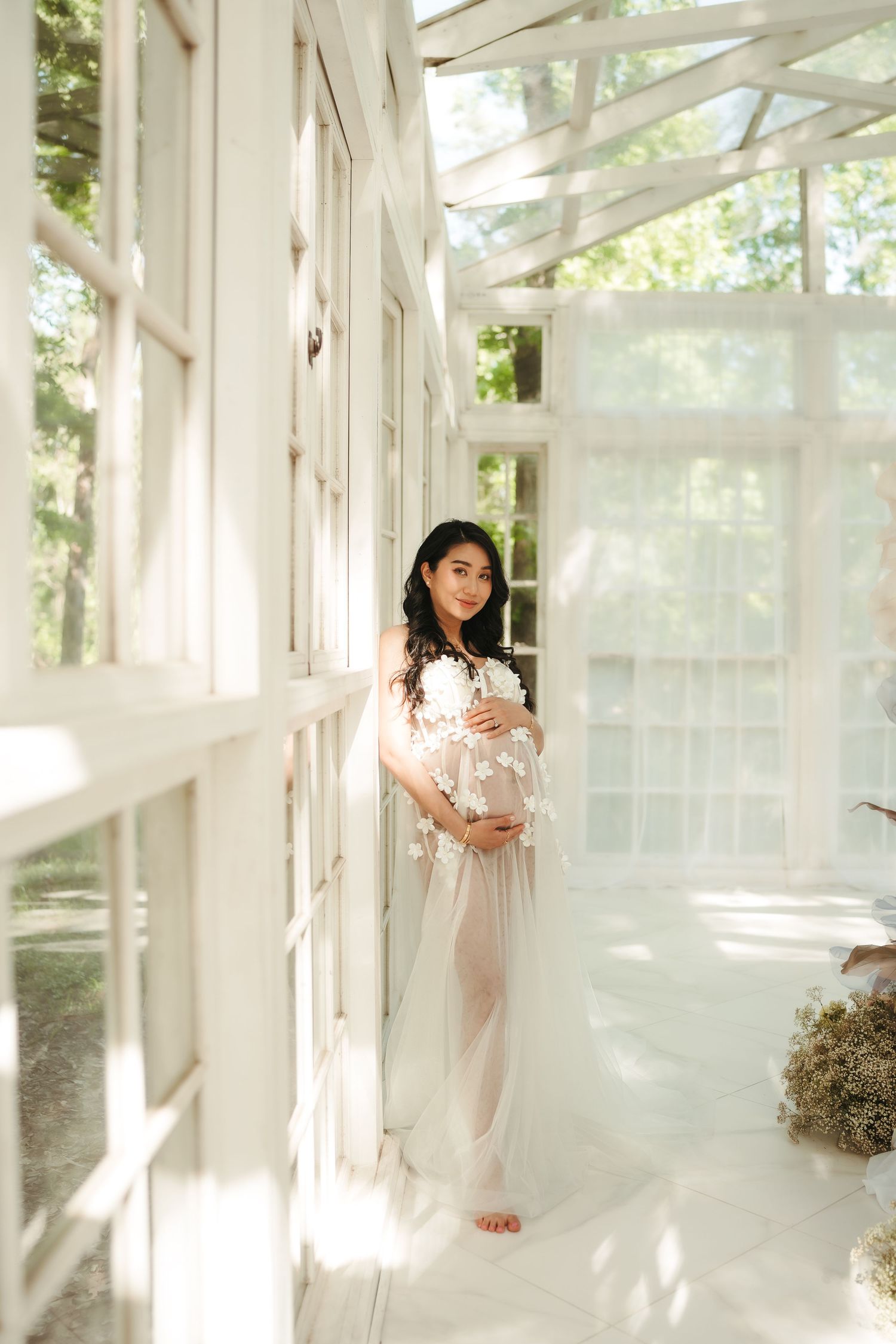 Ethereal photoshoot in sunlit greenhouse with flowing white dress.