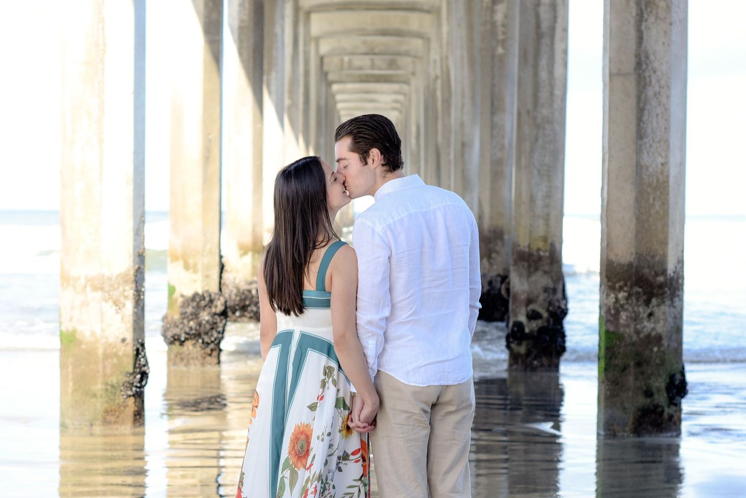 Seaside maternity photo under architectural pillars with ocean waves.