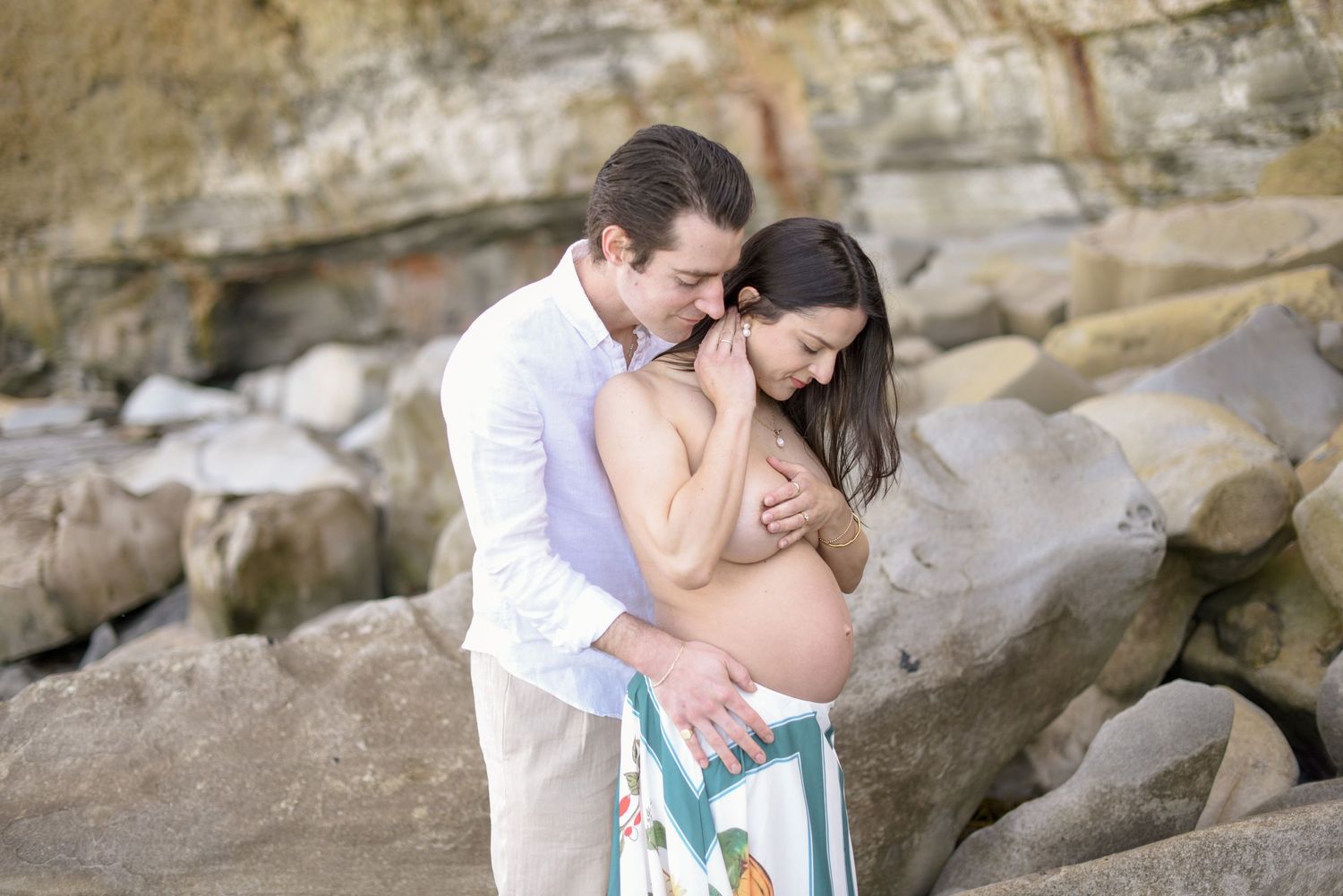 Romantic maternity moment captured against rocky coastal backdrop.