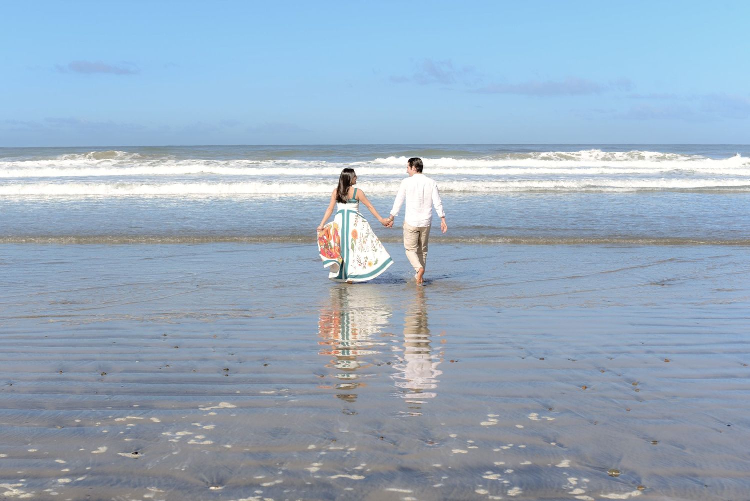 Two people strolling together on wet sand with ocean waves in the background.