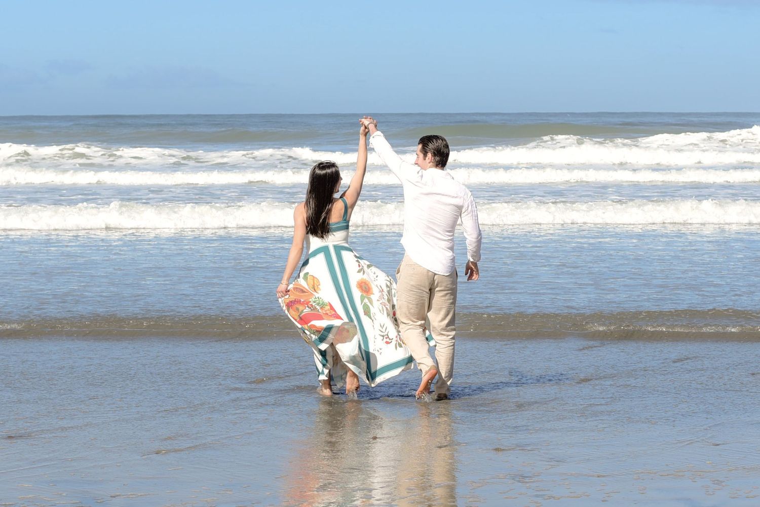 Couple walking hand in hand along the ocean shoreline at sunset.