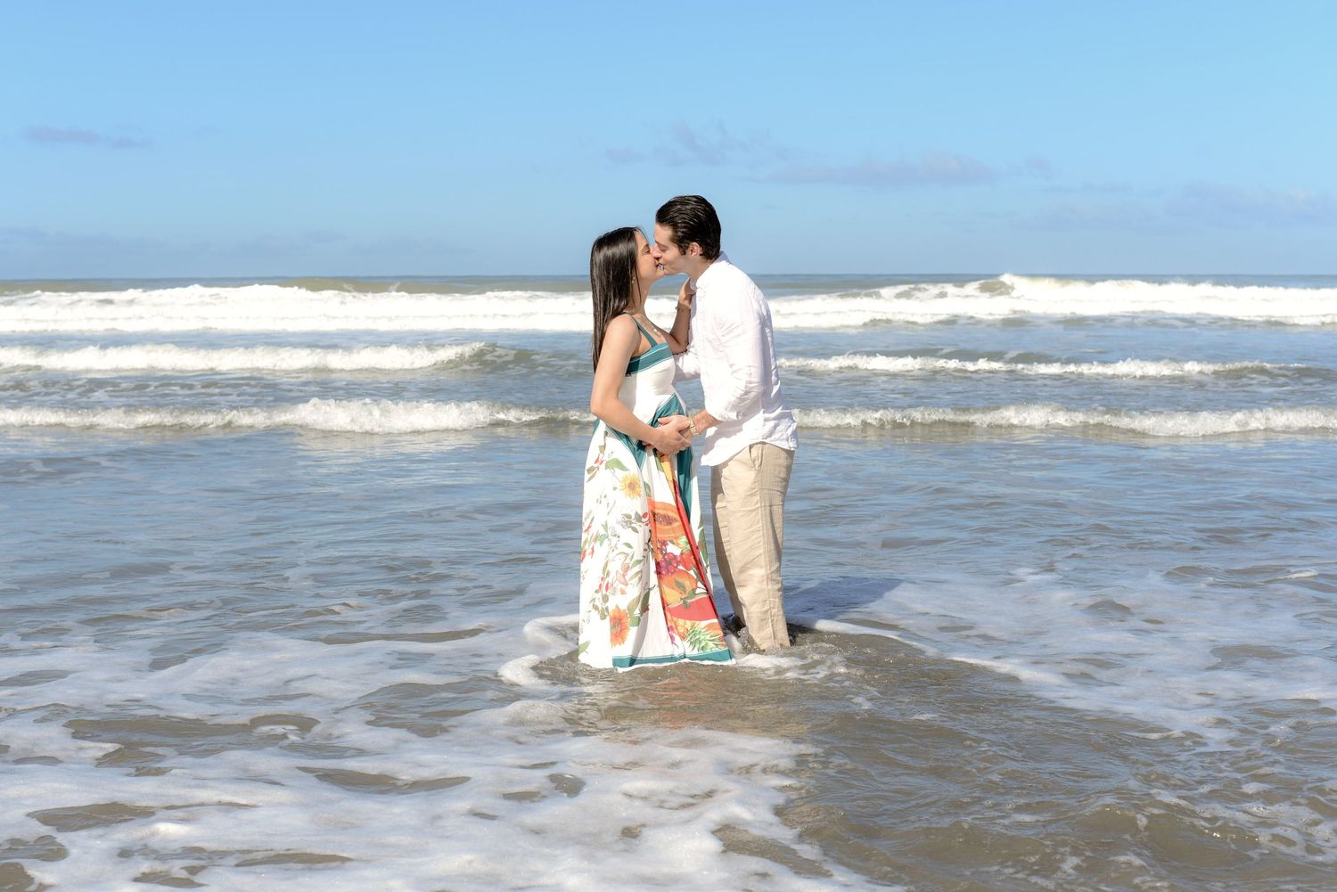 Couple embracing in shallow ocean water with waves crashing behind them.