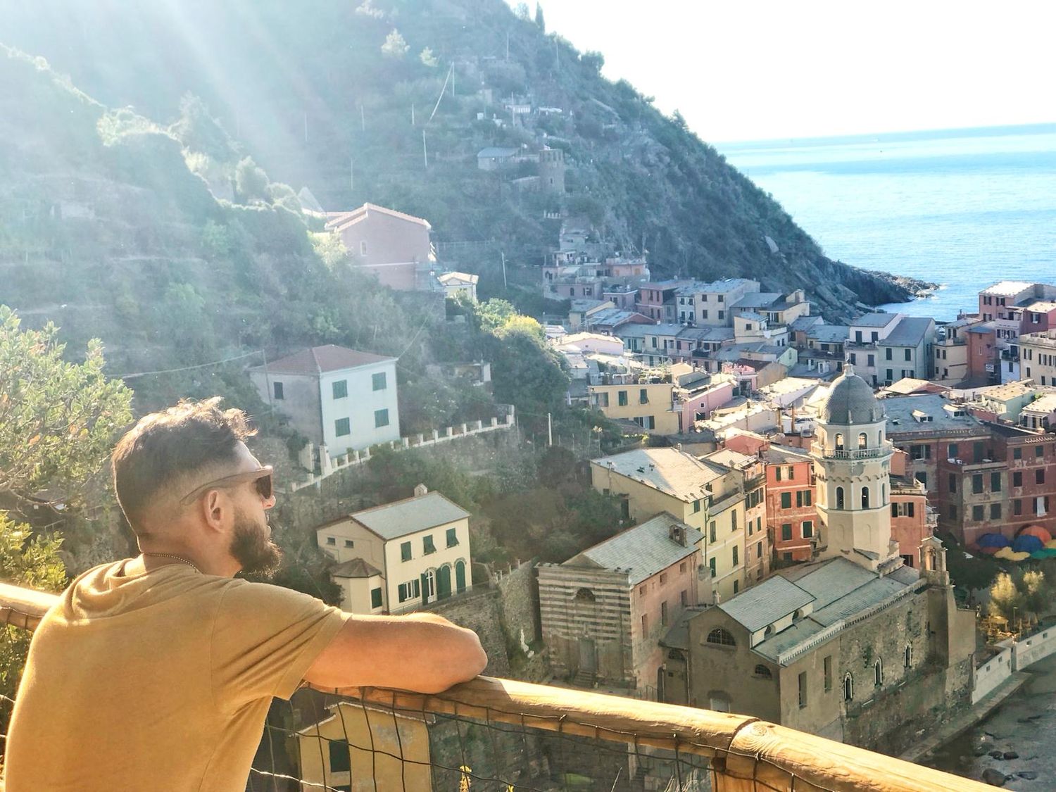 Person overlooking the colorful coastal buildings of Cinque Terre in Italy at sunset.