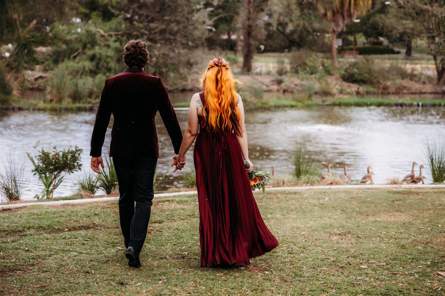 A graceful figure in a flowing blue gown stands near a serene lake as a black swan glides by on the grassy shore.