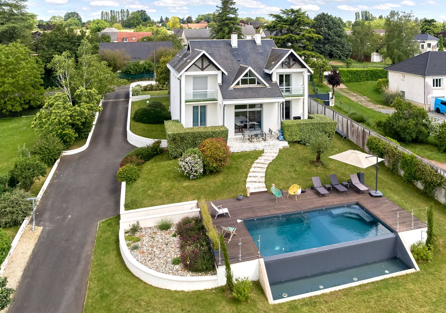 Aerial view of a modern residential property with a luxurious swimming pool and landscaped backyard surrounded by greenery.
