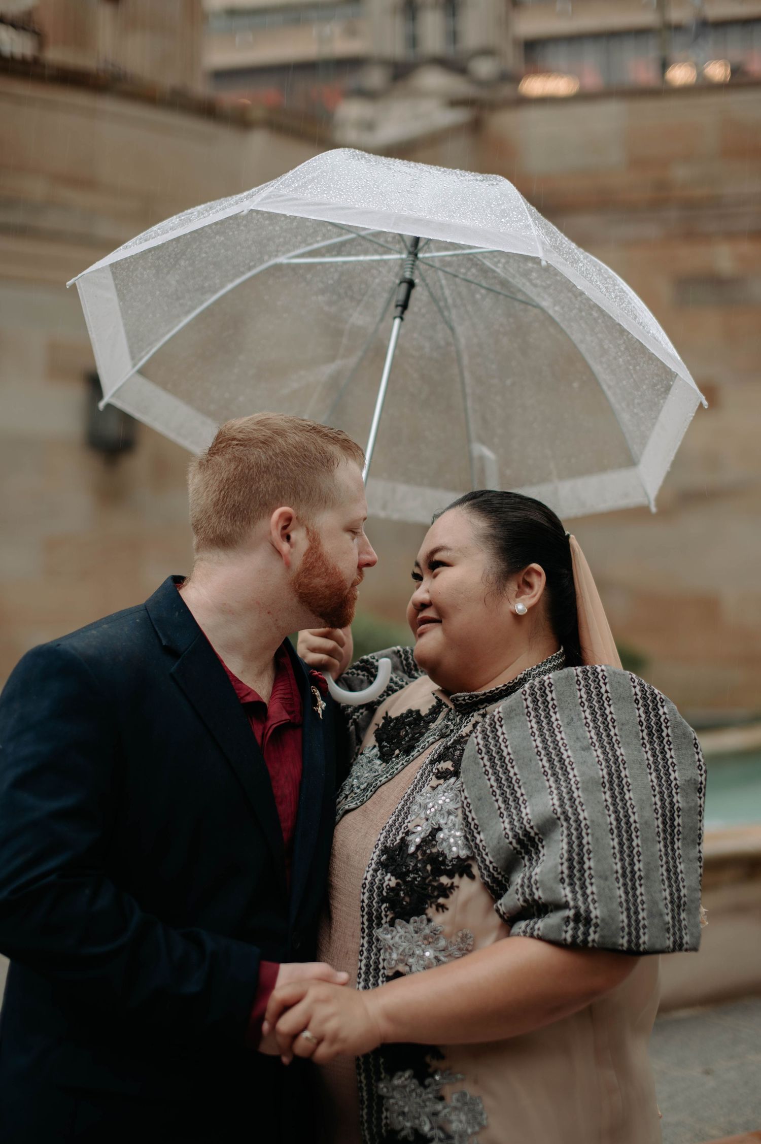 A couple embraces intimately under a clear umbrella in a romantic photoshoot sequence.