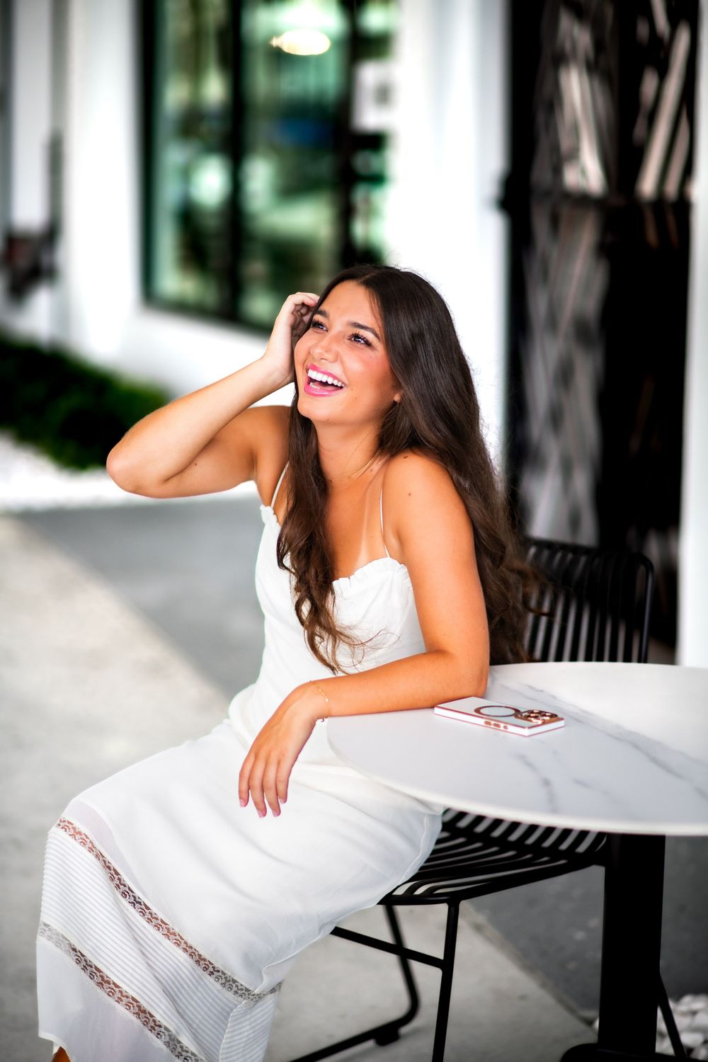 A model reclines on a white outdoor couch near a modern building with natural lighting.