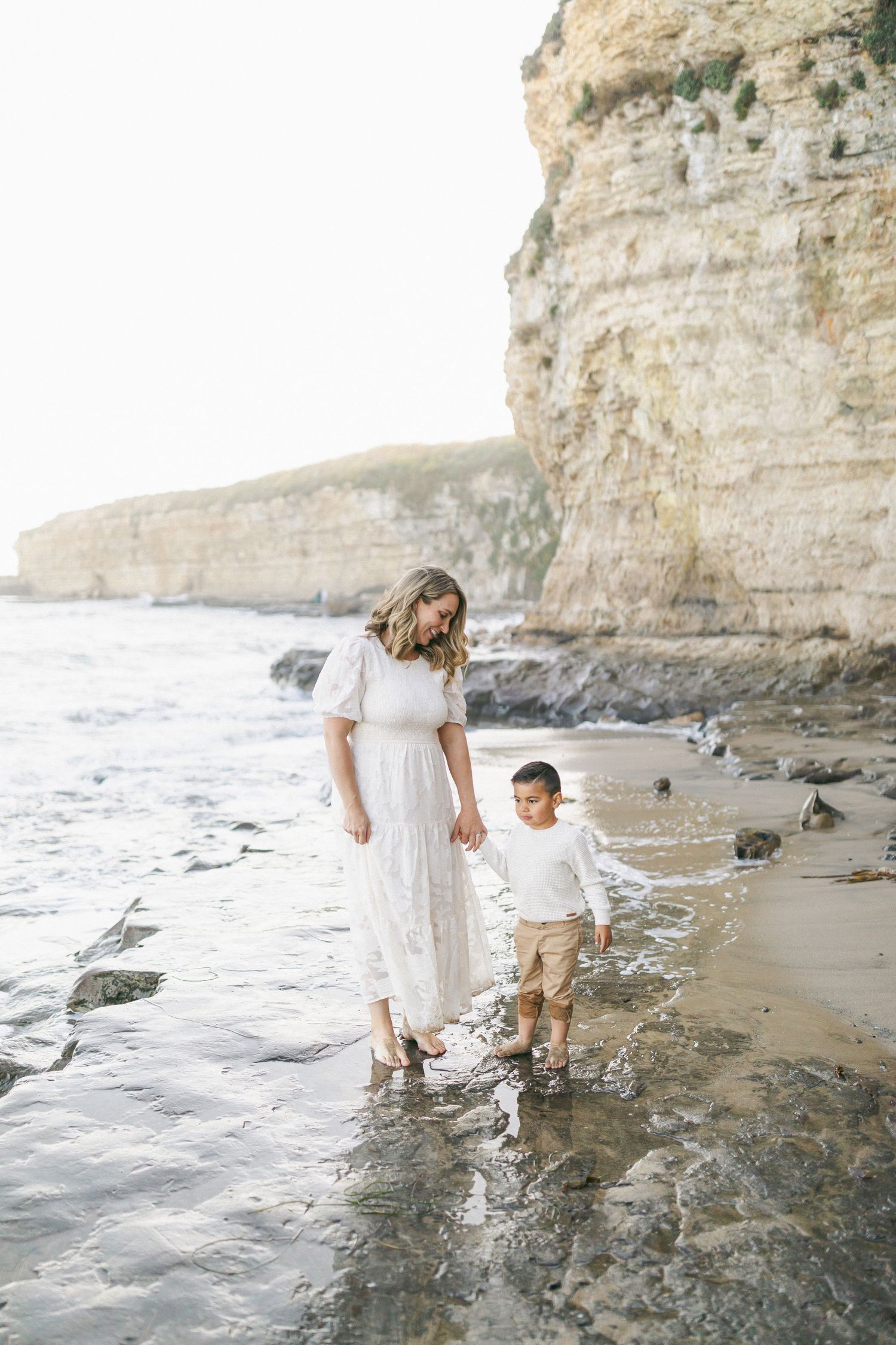 A pair of people splash in the waves at a scenic beach with towering limestone cliffs in the background captured on film by Chelsee Rawe