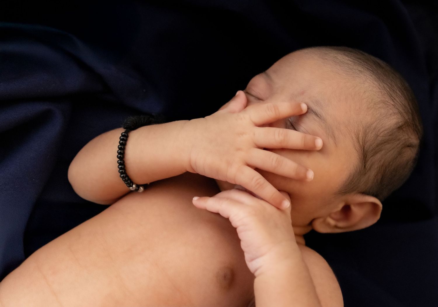 Adorable newborn baby covering face with tiny hand, capturing precious early moments of infancy and newborn photography
