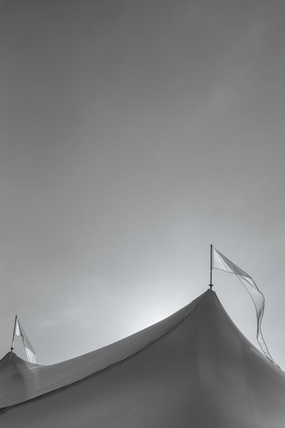 Black and white photo of a large tent top with white flags waving against an overcast sky.