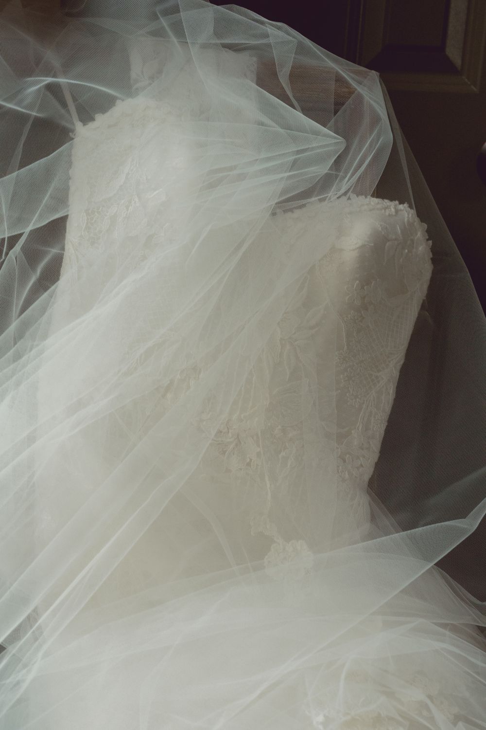 Elegant white lace wedding dress draped with flowing tulle veil fabric on display.