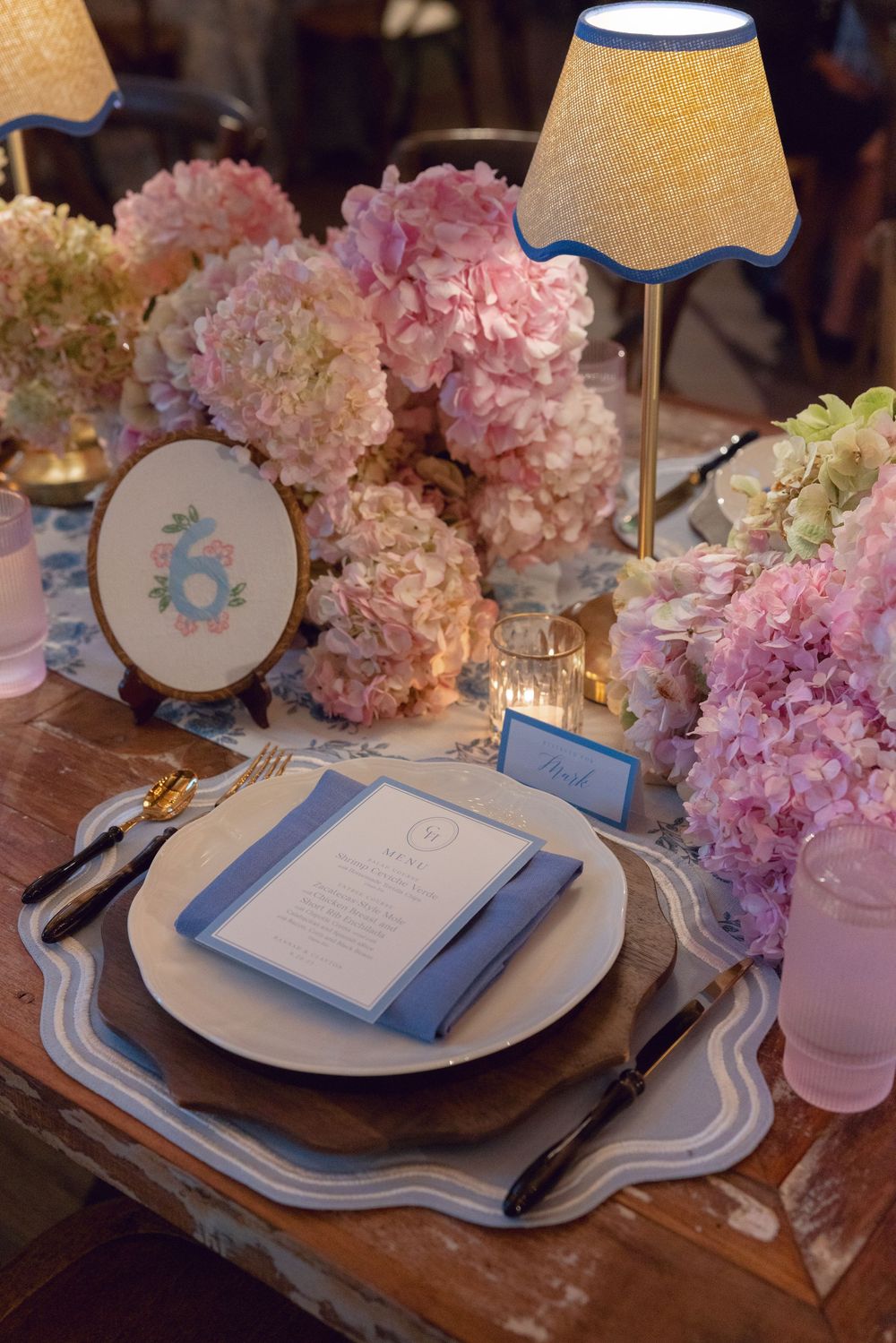 Elegant table setting with pink hydrangeas, blue napkins, and white plates on a rustic wooden surface.