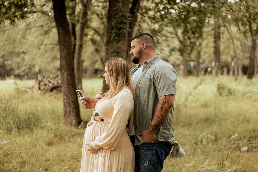 A couple shares a tender moment in a sunlit forest meadow, with the woman wearing a flowing cream dress.