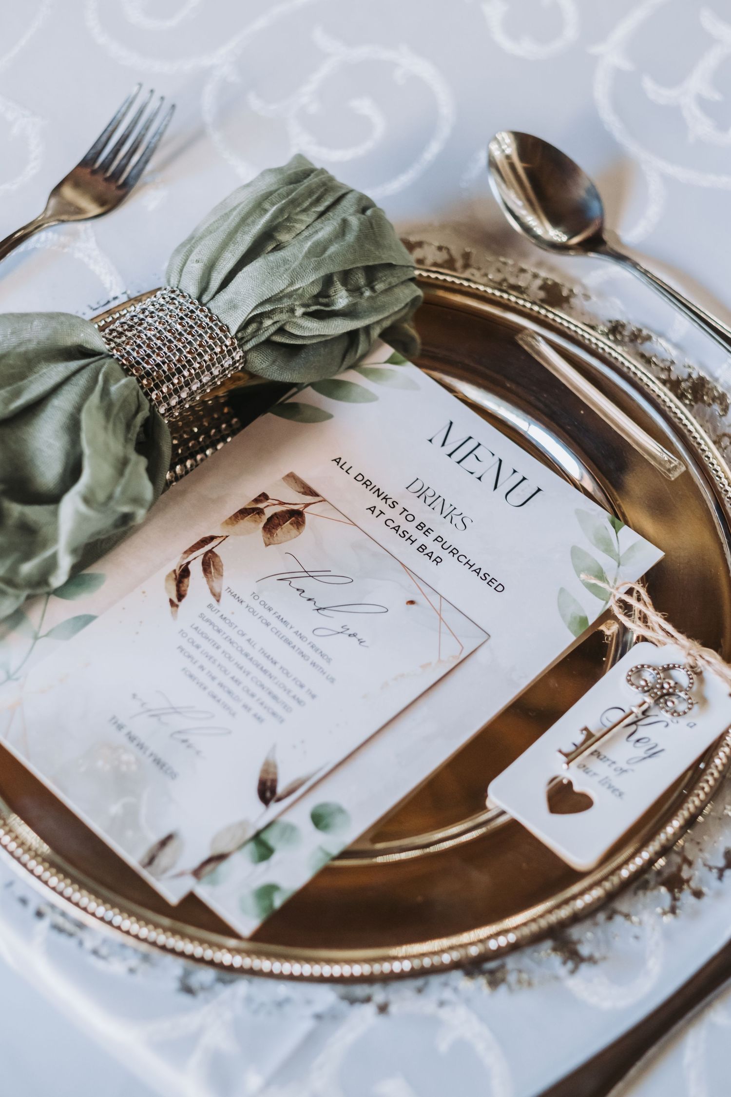 Elegant gold wedding place setting with sage green napkin, menu card, and botanical stationery details.