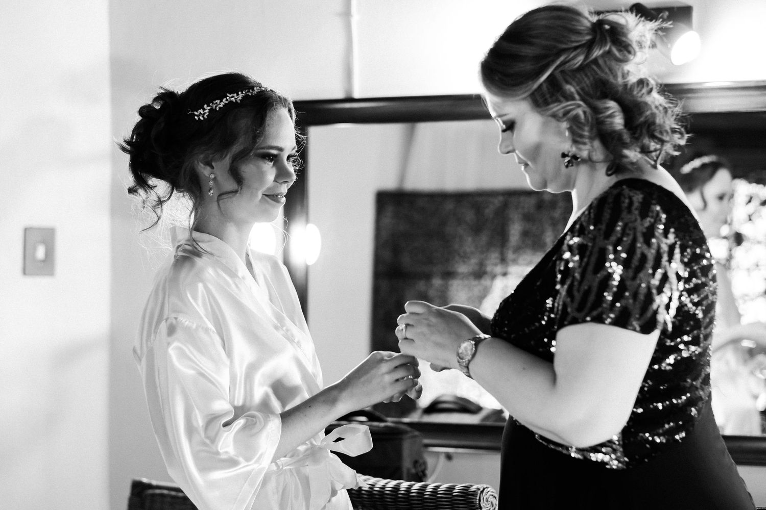 Black and white photo of a bride in a robe sharing a tender moment with her bridesmaid.