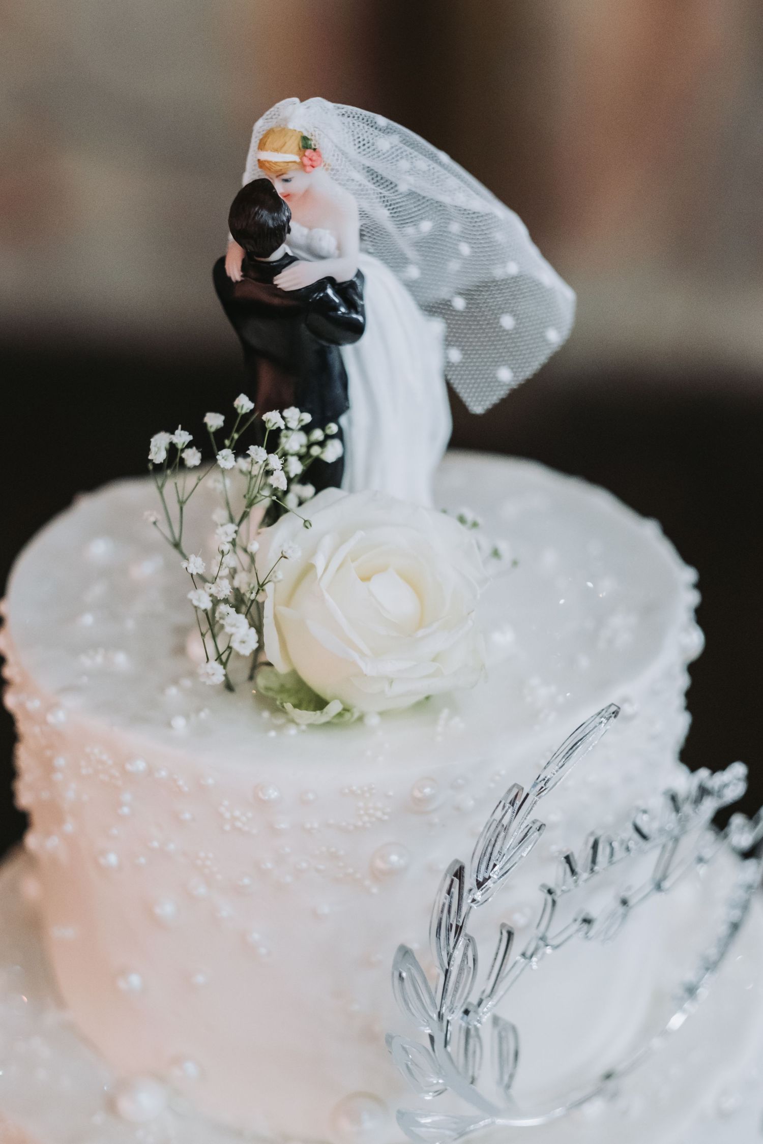 Close-up of bride and groom cake topper with white rose and baby's breath on a pearl-textured wedding cake.