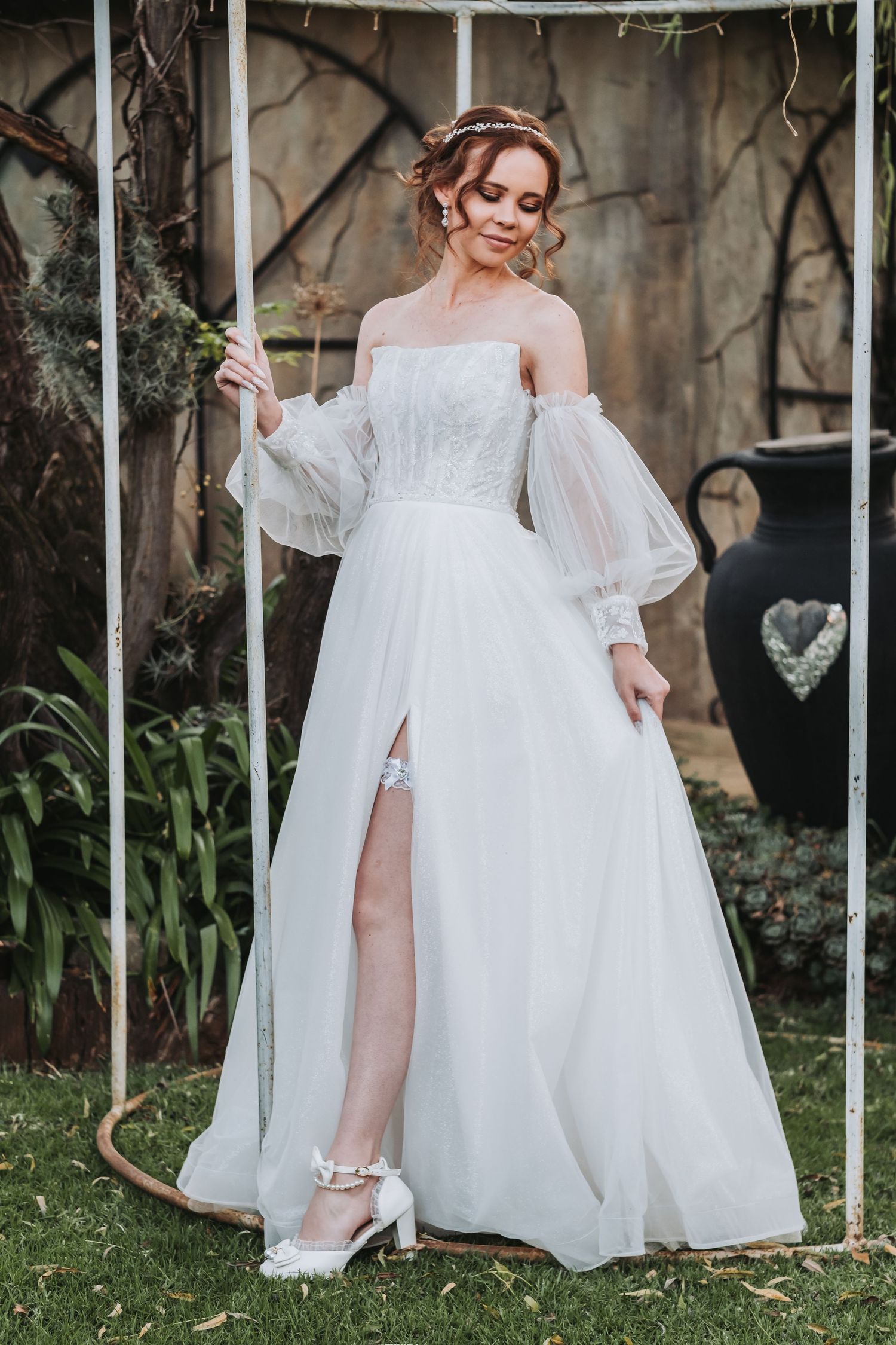 Bride in elegant off-shoulder white tulle ballgown with sheer puff sleeves posing in a garden wedding setting.