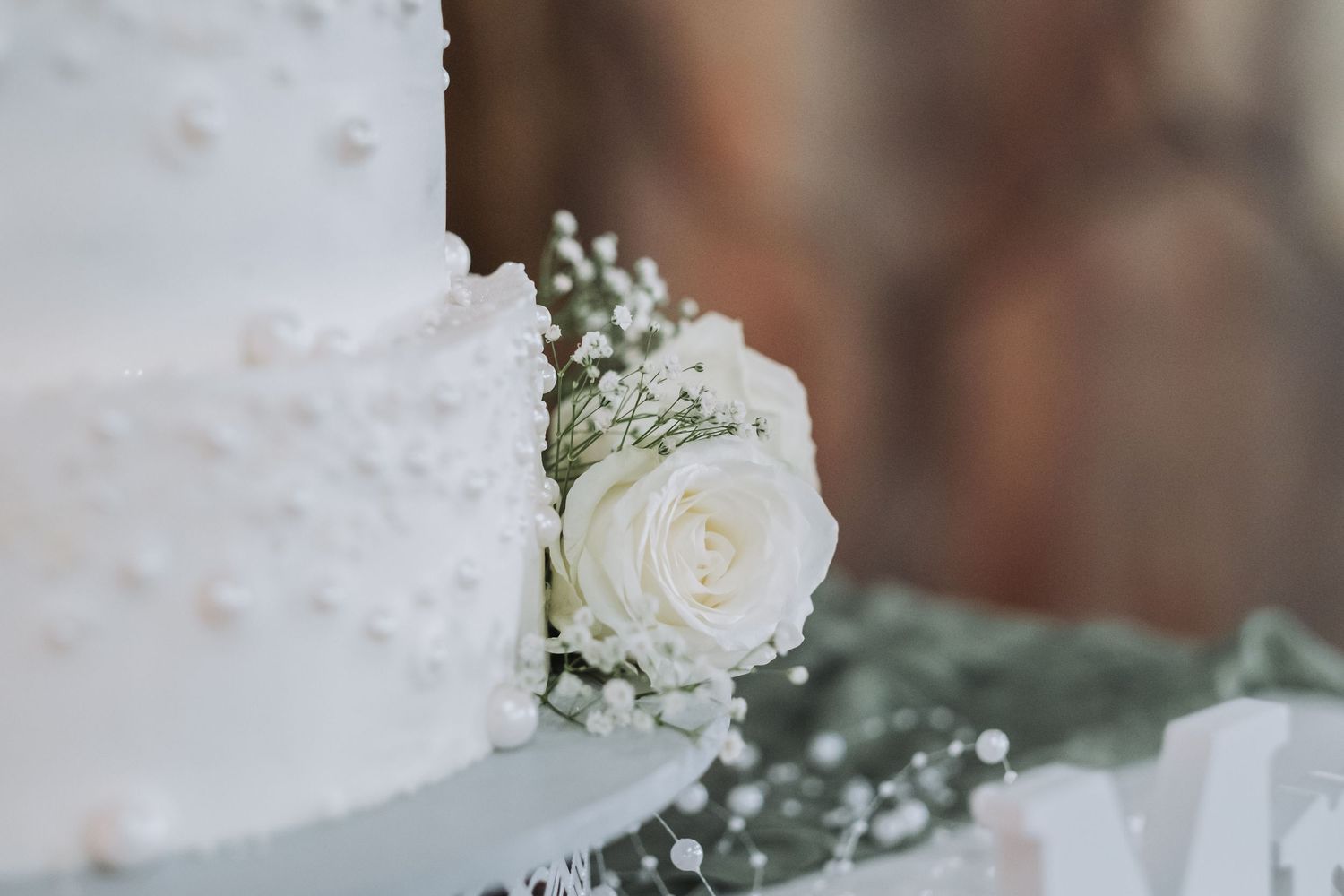 Elegant white wedding cake adorned with pearl details and fresh white roses and baby's breath flowers.