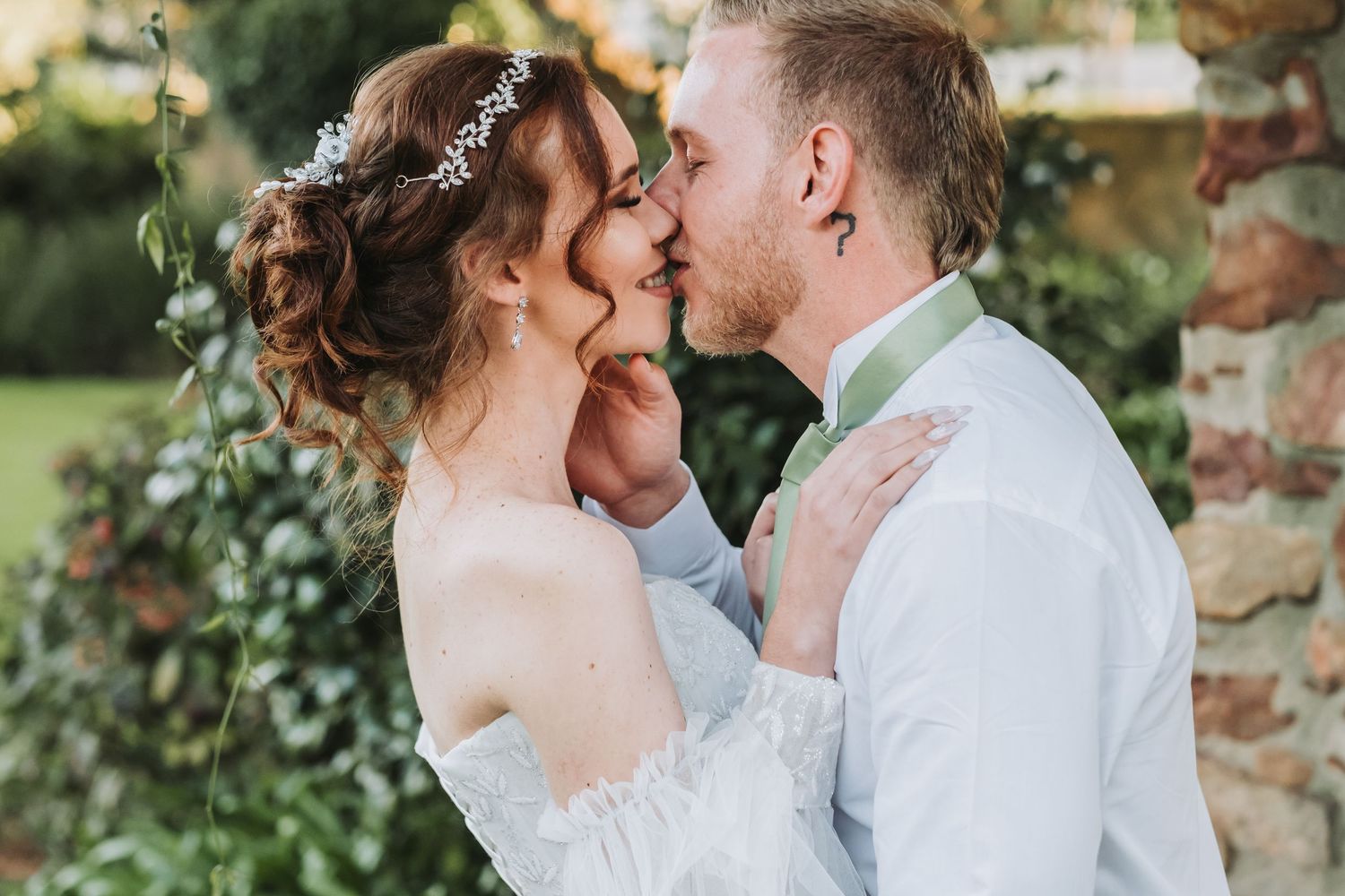 Bride and groom sharing a romantic kiss outdoors surrounded by lush greenery at their garden wedding.