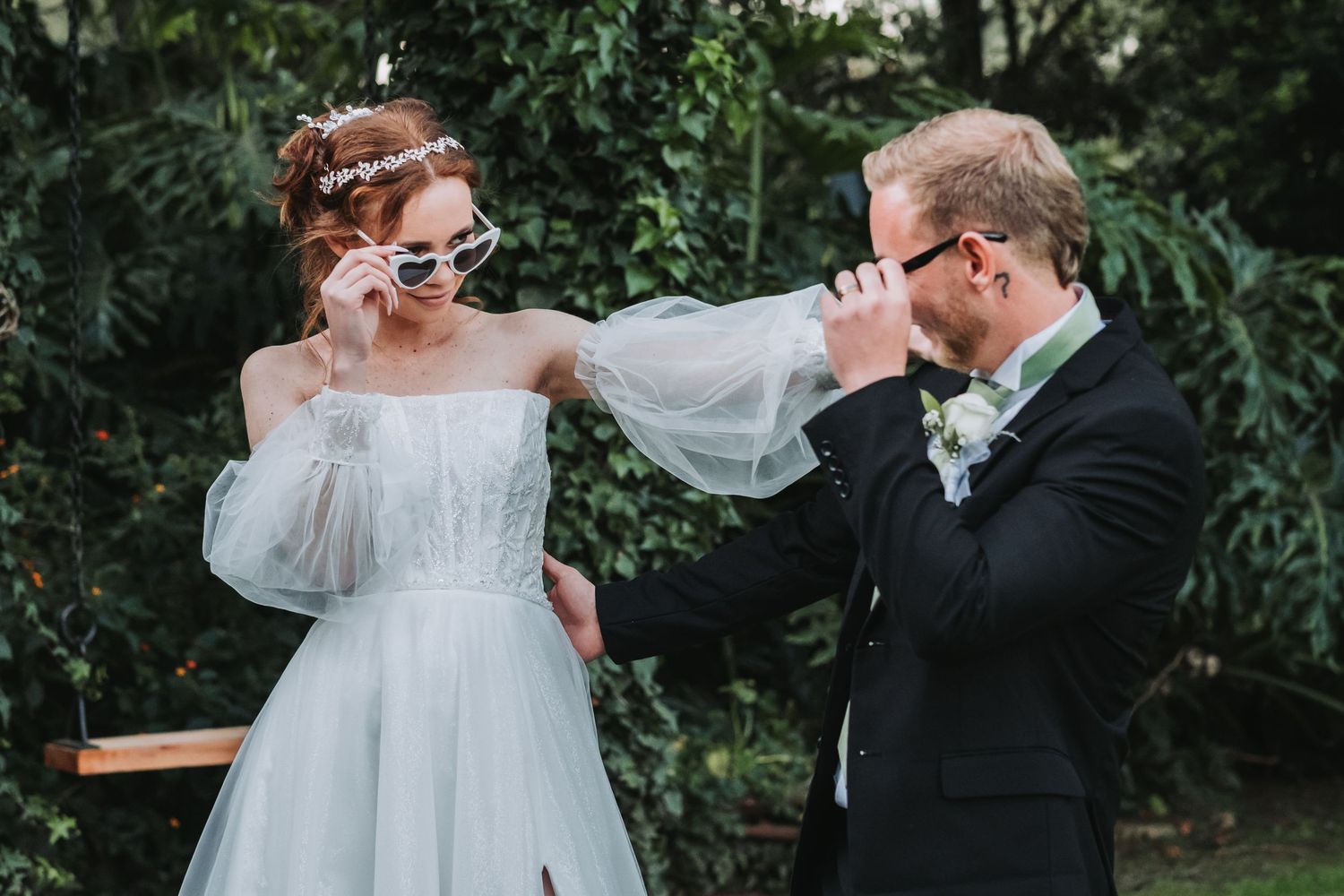Bride and groom playfully posing with sunglasses outdoors, sharing a fun moment on their wedding day.