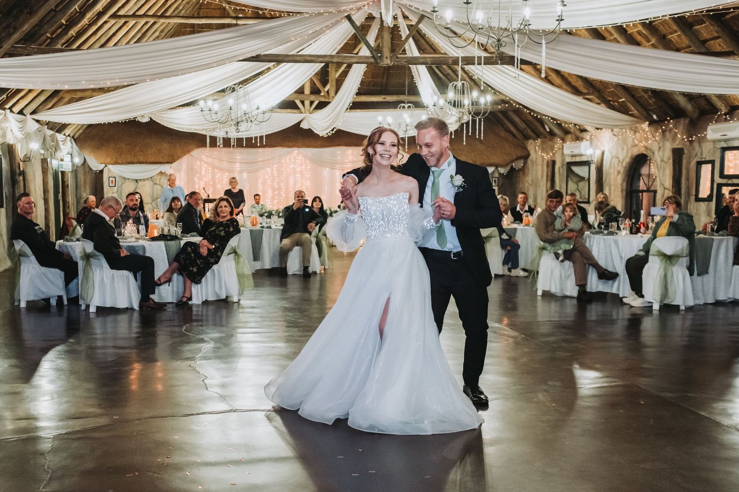 Bride and groom sharing their first dance in a beautifully decorated rustic wedding reception venue with guests watching.