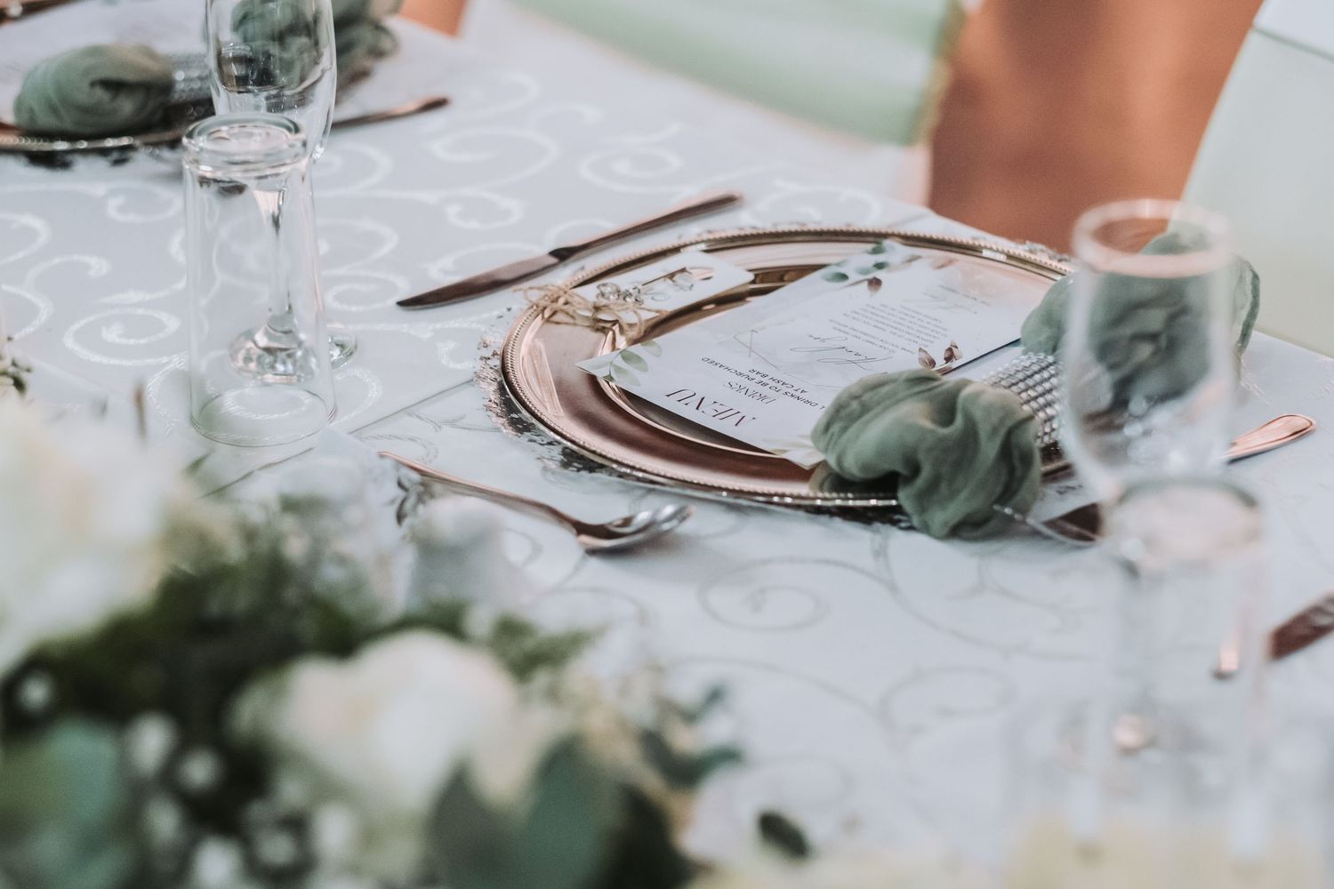 Sophisticated wedding table setting with gold charger plates, sage green napkins, and white floral centerpieces.