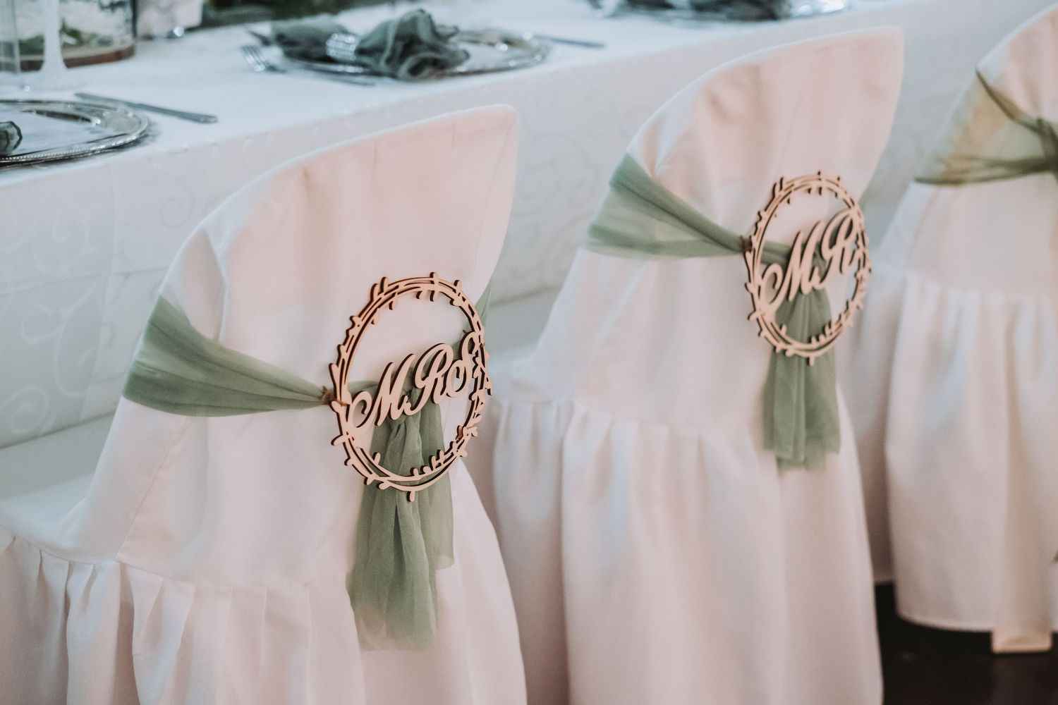 White wedding chairs decorated with sage green ribbon sashes and wooden Mr and Mrs signs.
