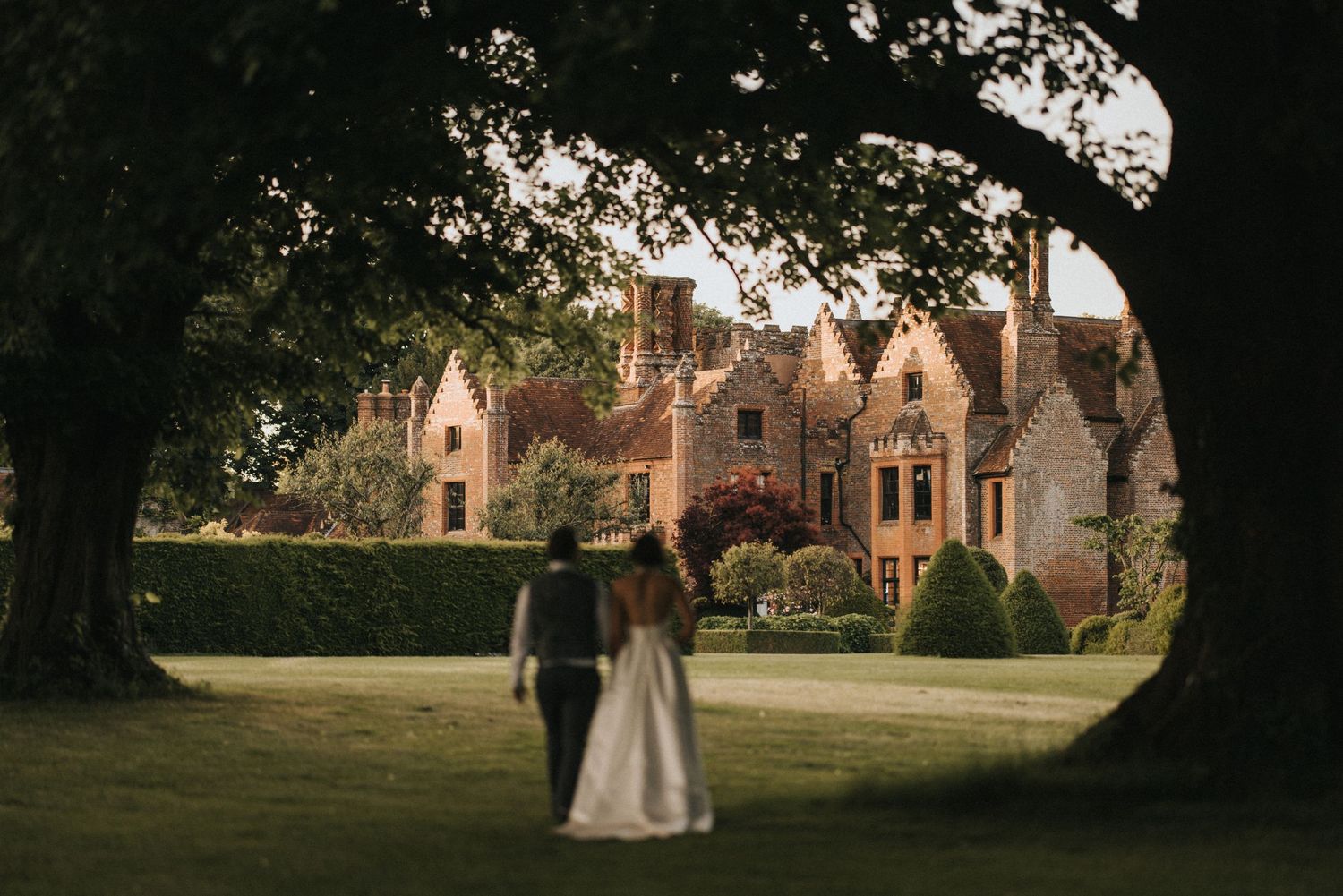 Aerial view of a historic Victorian manor house with red brick chimneys surrounded by manicured green lawns.