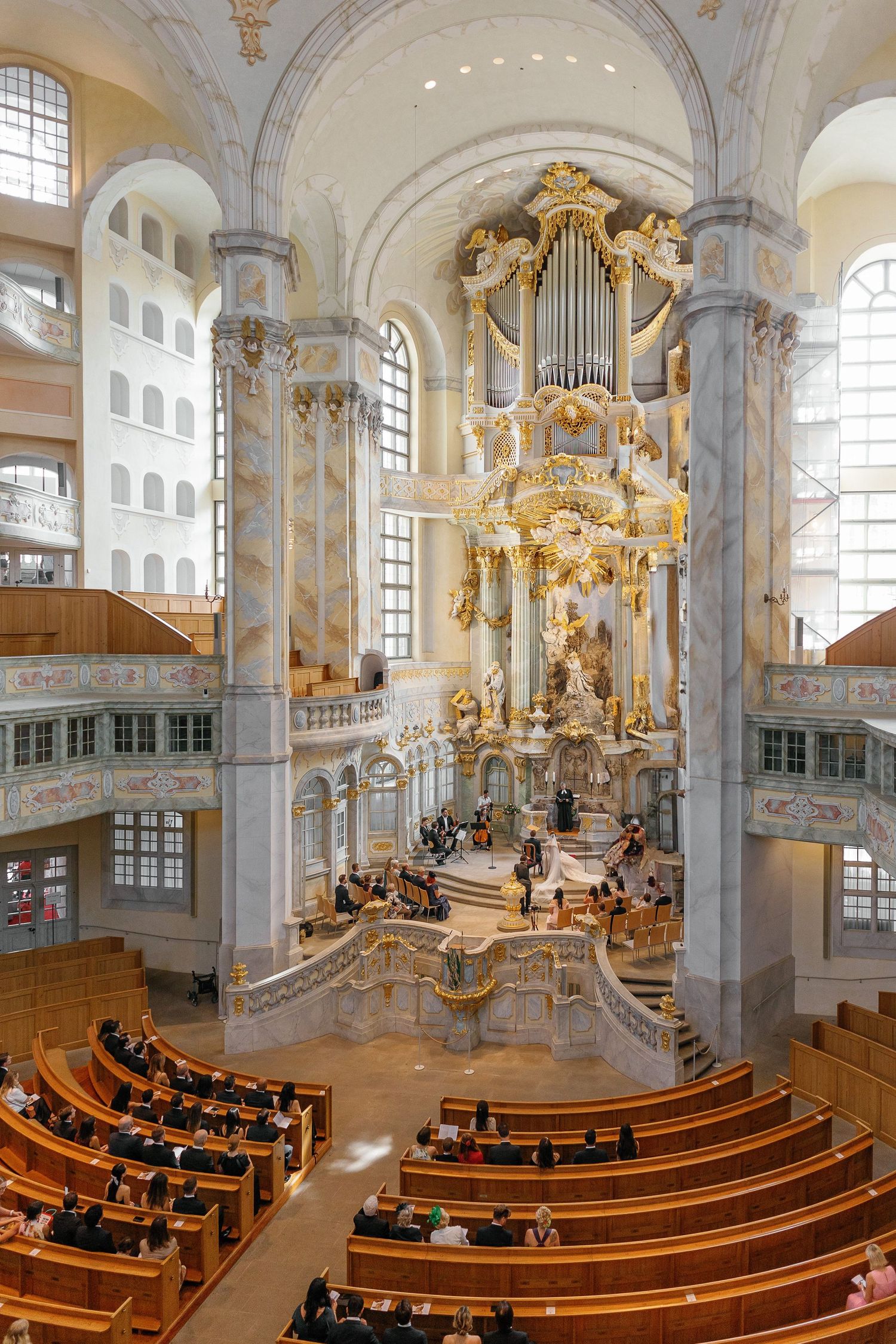Interior view of Dresden Frauenkirche with ornate Baroque altar, golden organ pipes and curved wooden pews.