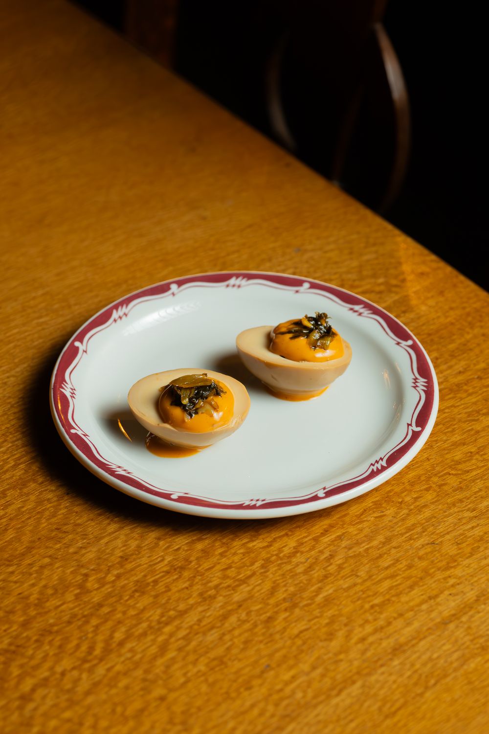 Two deviled egg halves garnished with caviar served on a white plate with red trim rest on a wooden table.