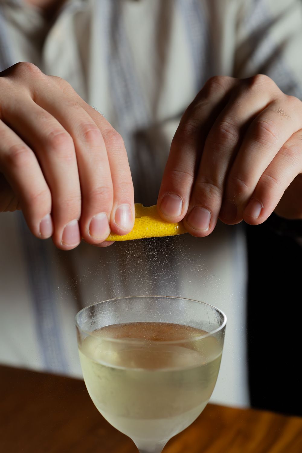 Hands squeezing fresh citrus over a coupe glass filled with a clear cocktail.