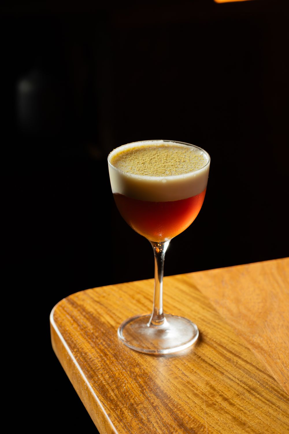 A sequence of cocktail glasses filled with amber-colored drinks displayed on a wooden surface in warm lighting.