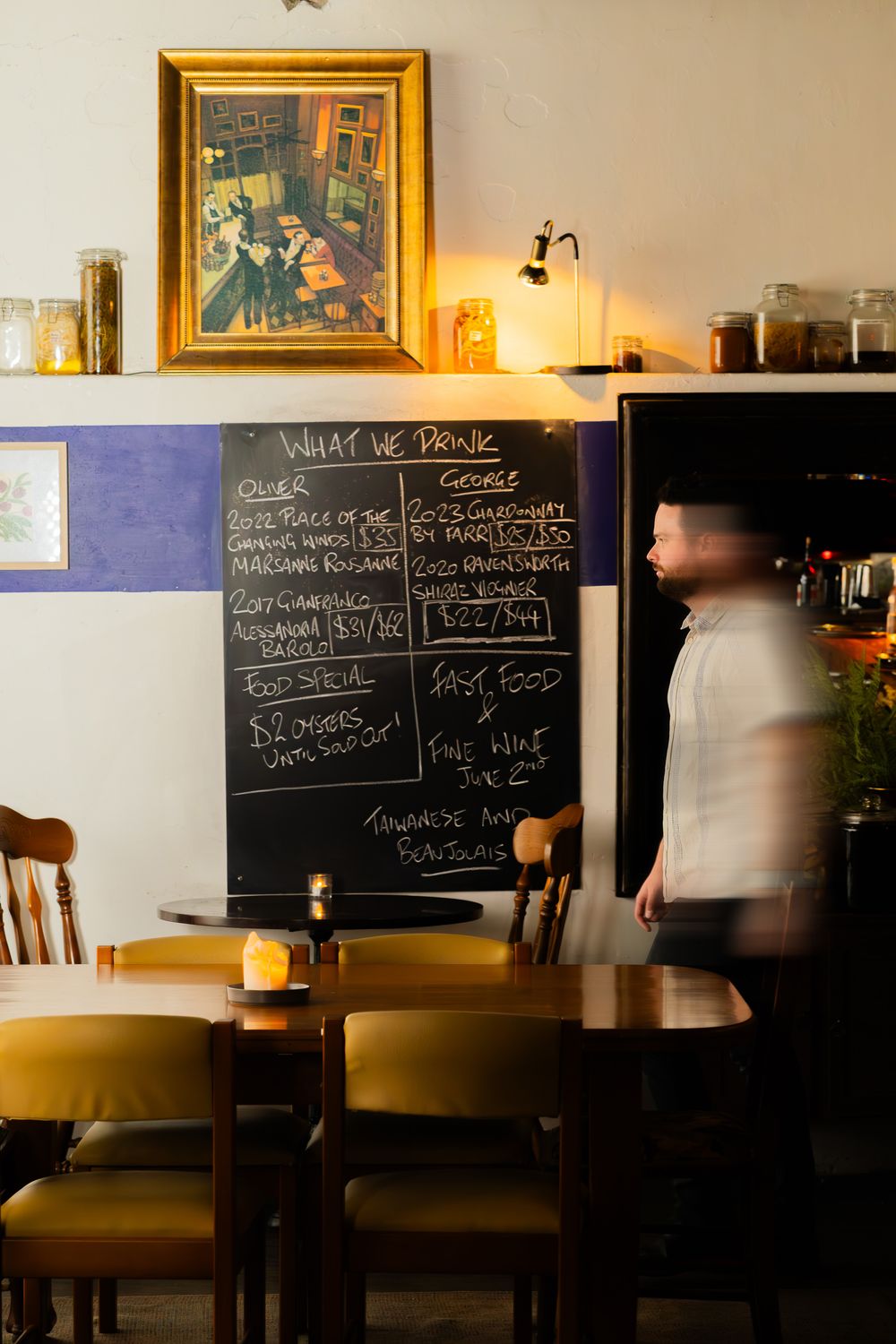 Interior of dimly lit restaurant with wooden tables and blackboard menus mounted on wall creating cozy ambiance.