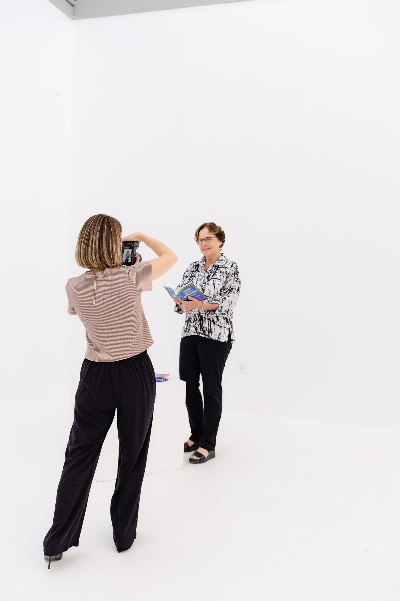 Photographer taking pictures of a subject against a white background in a minimalist studio setting.