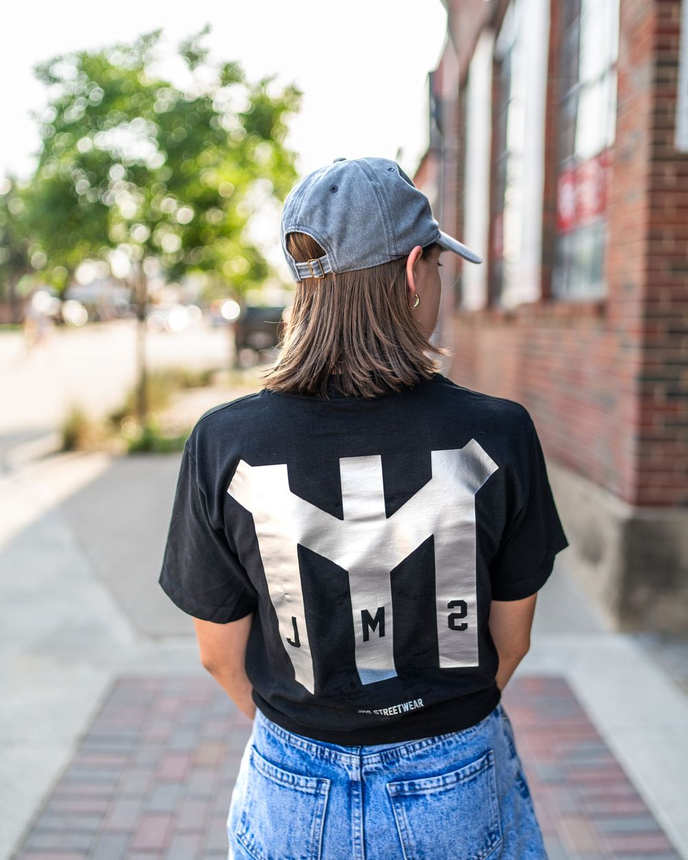 Photo of teenage female walking away from camera wearing a JMS Streetwear t-shirt and jeans.  Photo by Brian Balloon