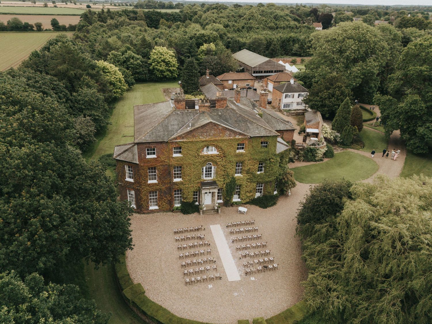 Aerial view of a classic Georgian manor house with a stone driveway and rows of chairs set up for an outdoor event.