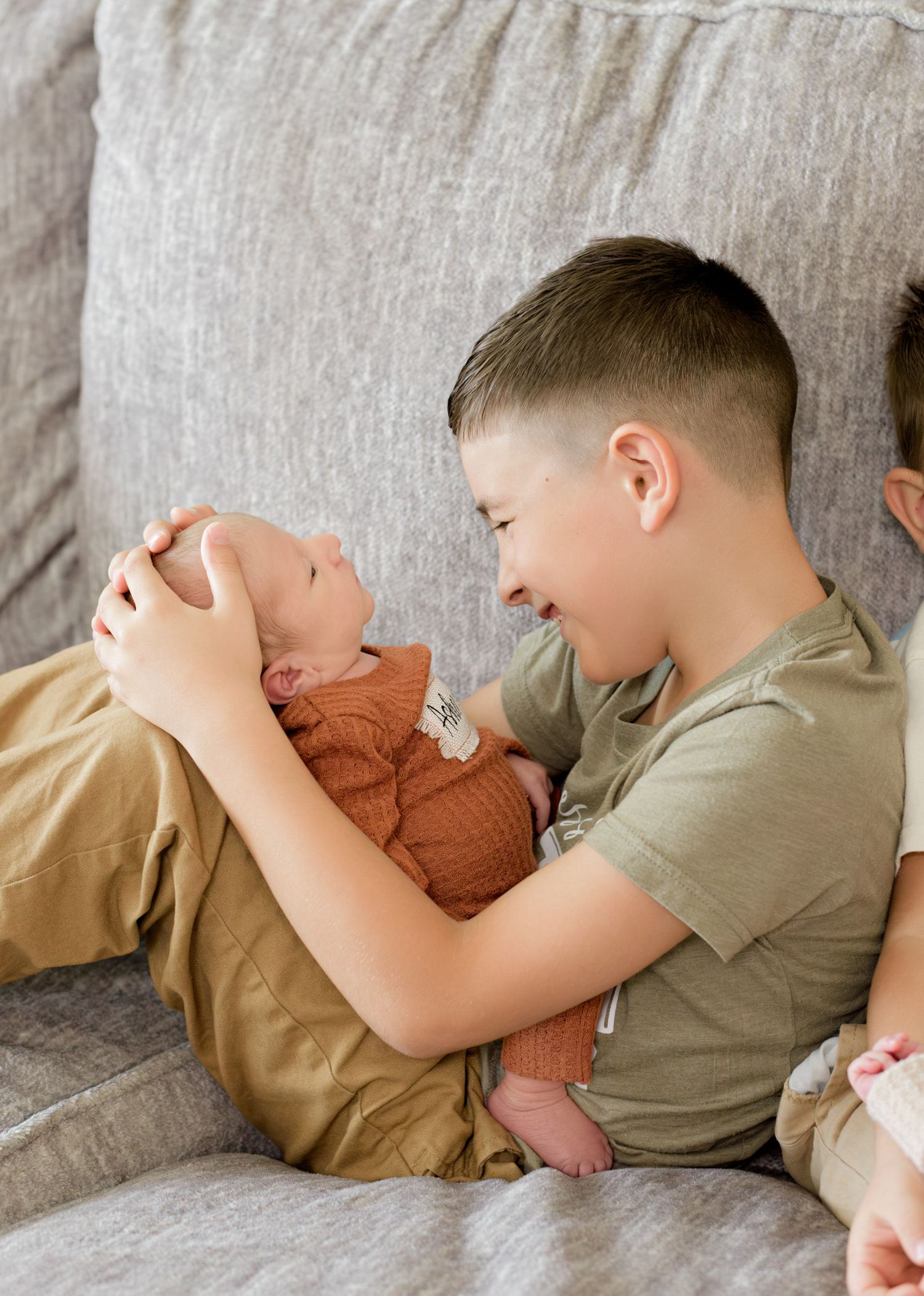 Young child and baby sharing a joyful bonding moment while lounging on a gray couch together.