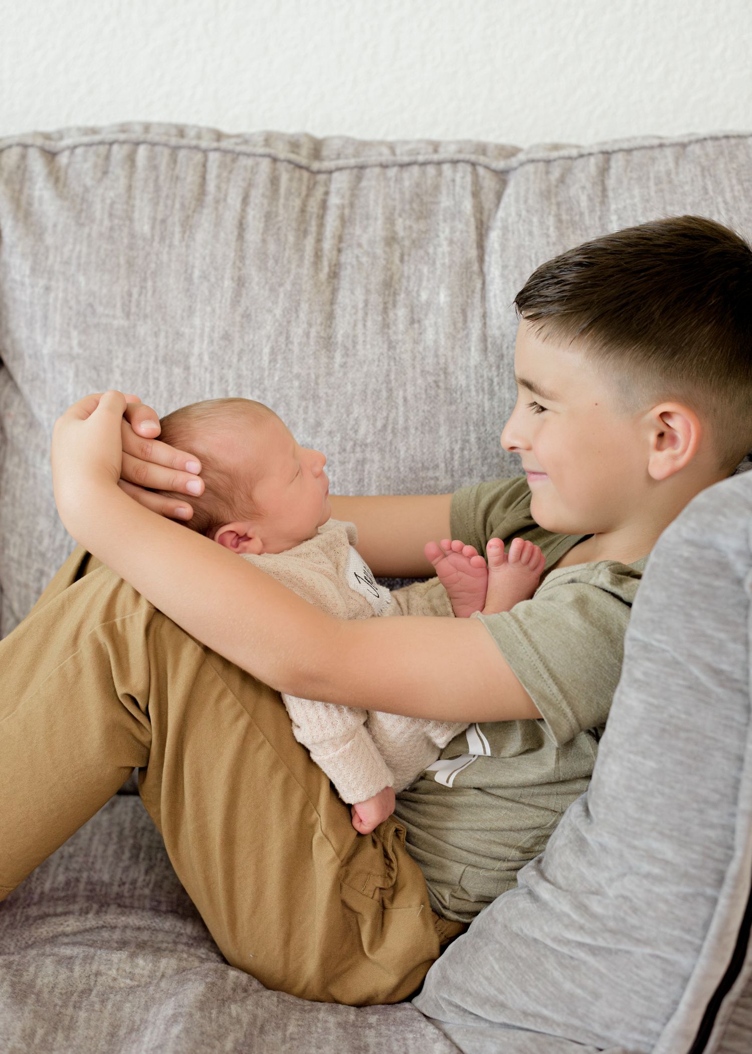 Siblings playing and interacting together on light colored couch in living room.