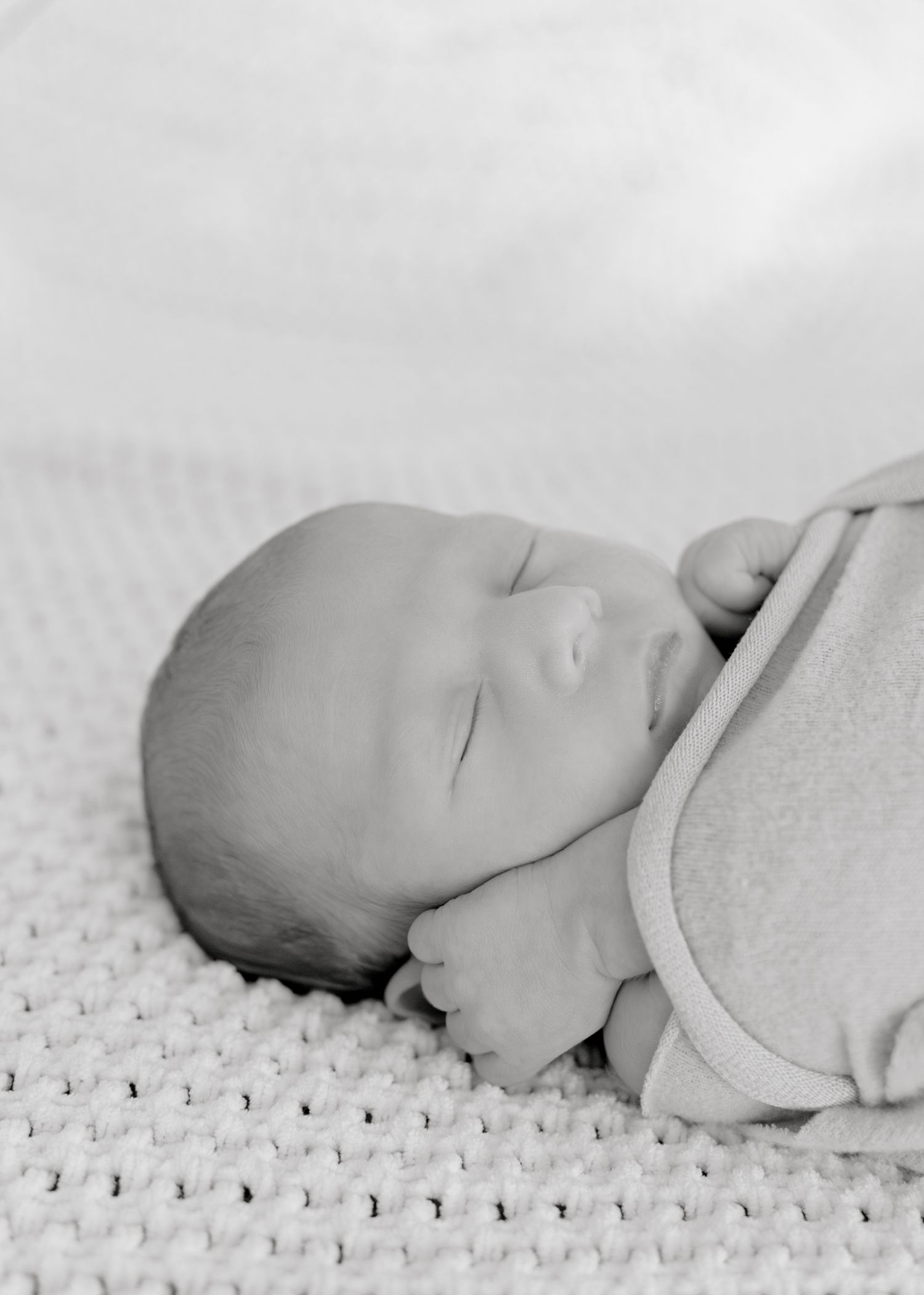 Close-up black and white portrait of a peaceful sleeping newborn on textured fabric.