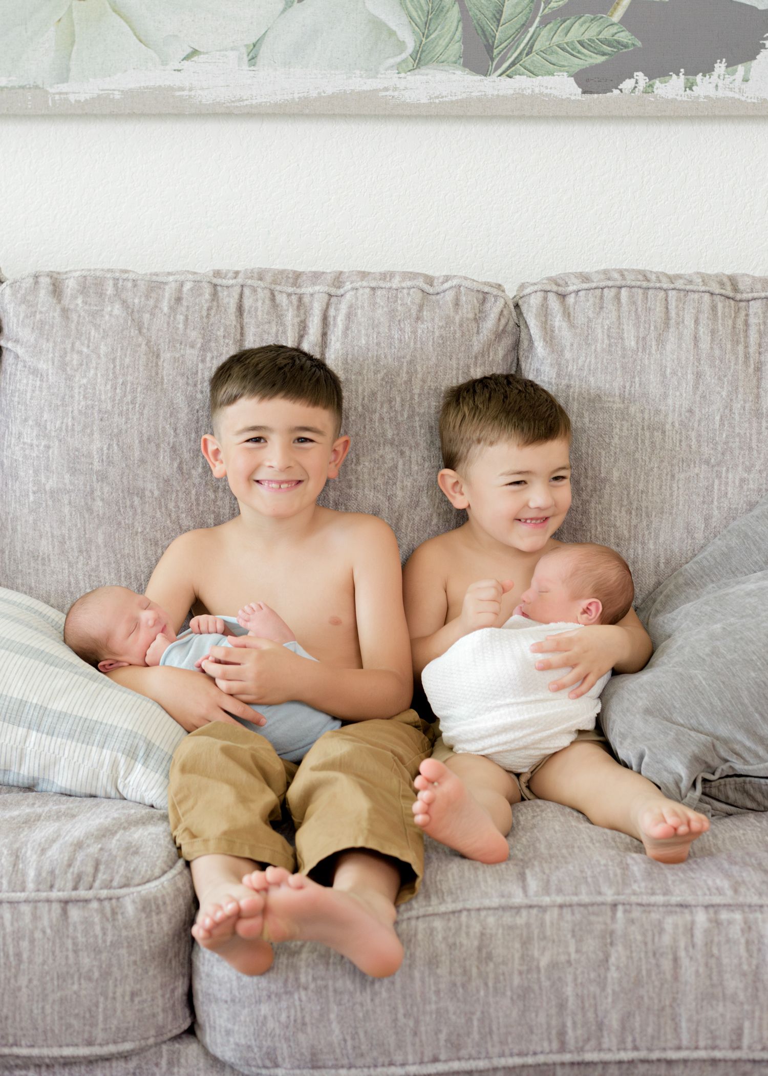 Two young children share playful moments while lounging together on a gray couch.
