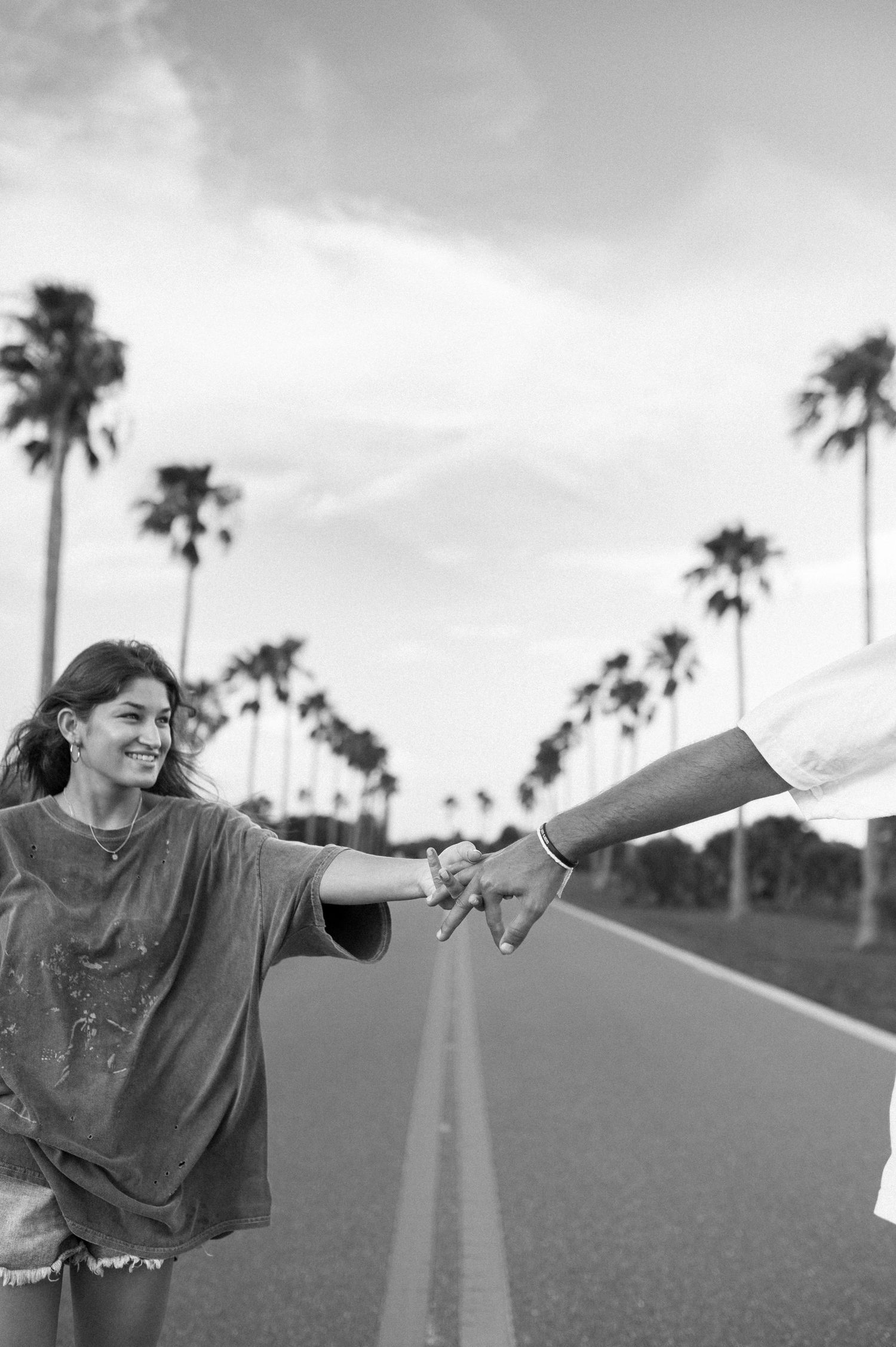 Black and white photo of joyful person reaching out on palm tree-lined road.