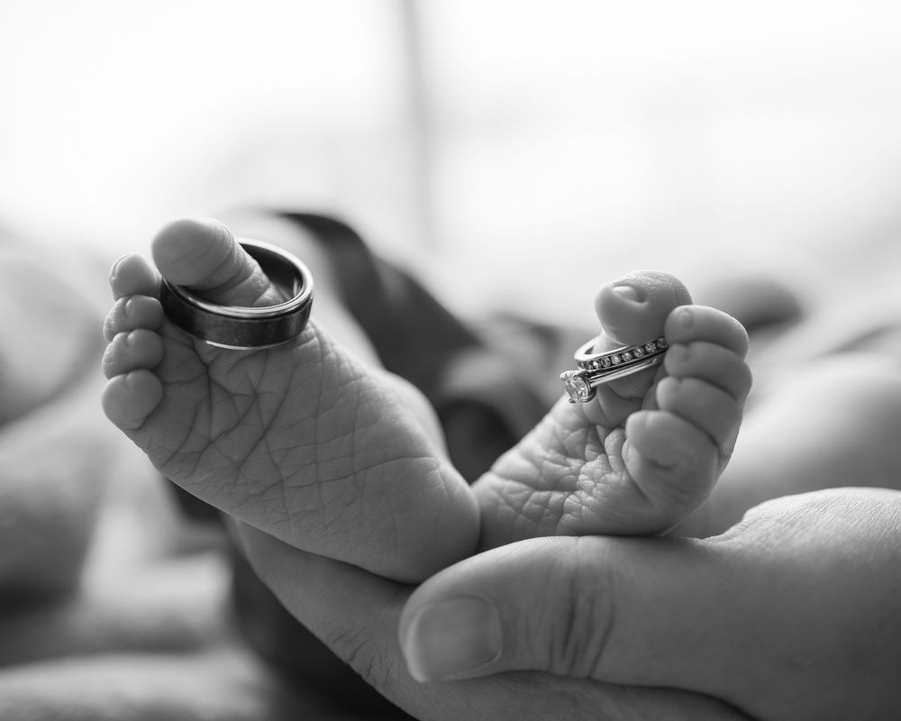 Black and white photograph of a tiny newborn baby foot being gently cradled in an adult's hand.