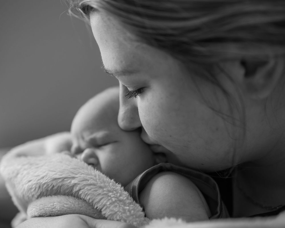 A tender black and white photograph of a mother and sleeping baby sharing an intimate bonding moment.