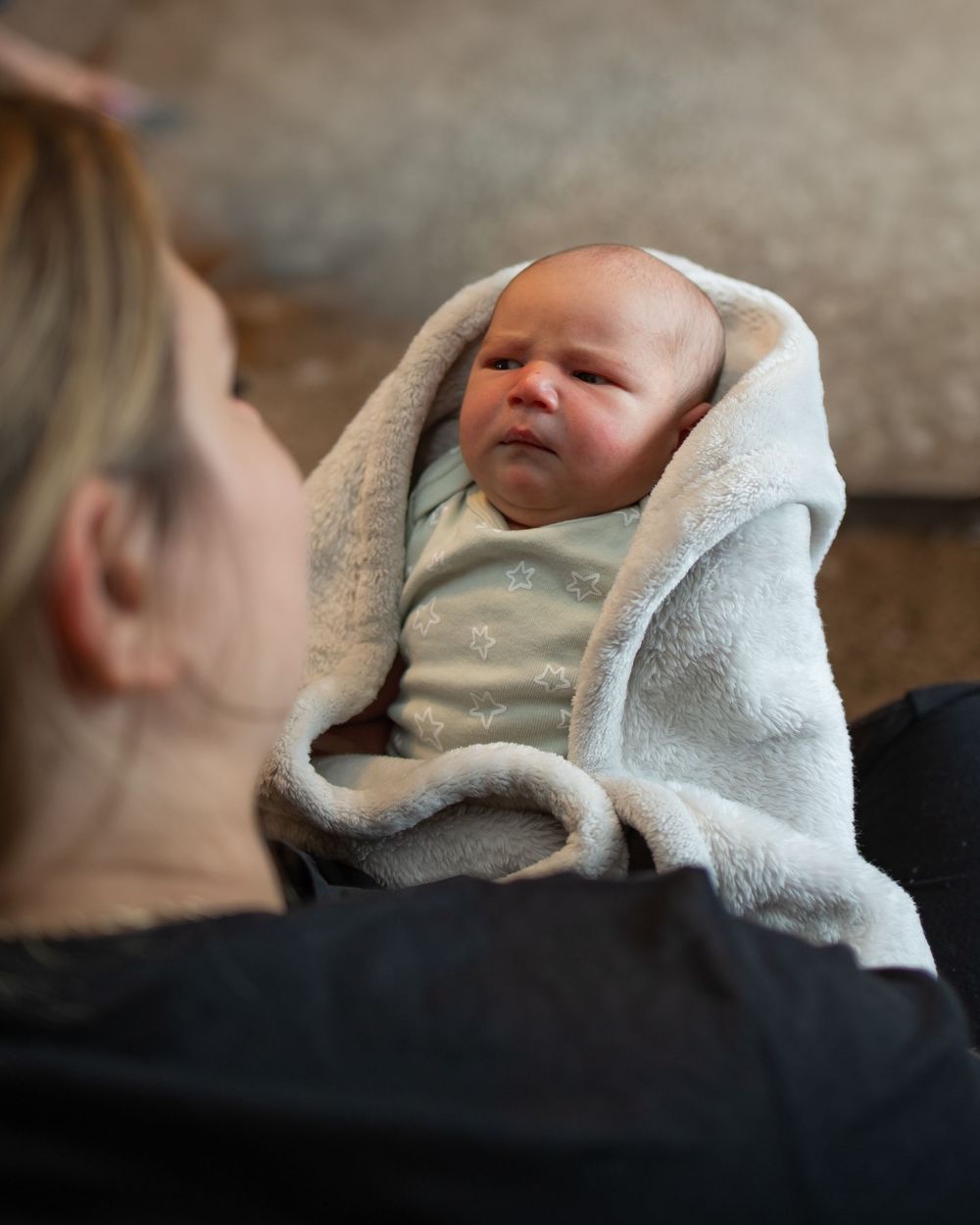 A tiny infant wrapped in a soft white blanket rests peacefully on a caregiver's lap.