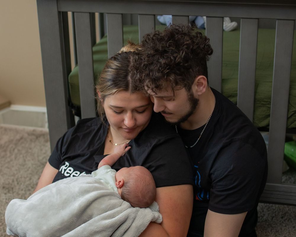 A couple tenderly holds their newborn baby while sitting on a porch bench.